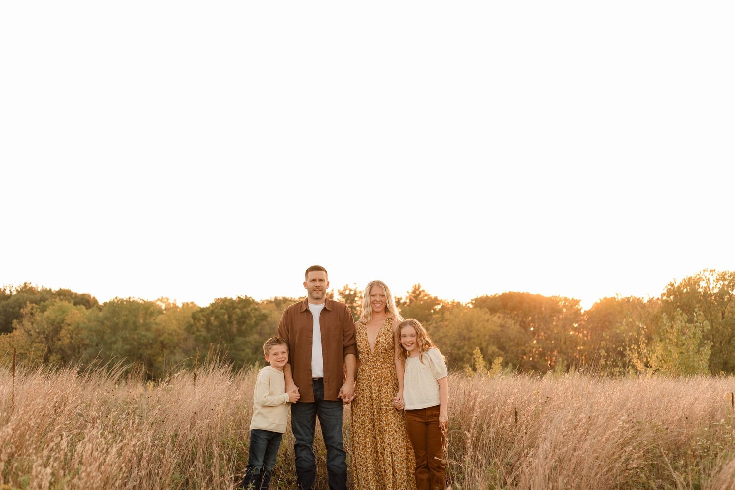 A family stands together in a golden field at sunset with tall grass and trees in the background.