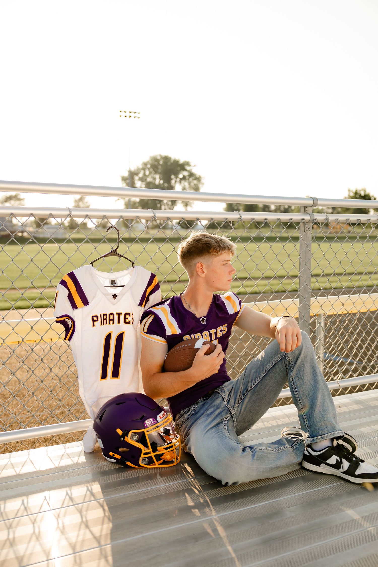 High school football player sits on bleachers with Pirates team jersey and purple helmet beside him.