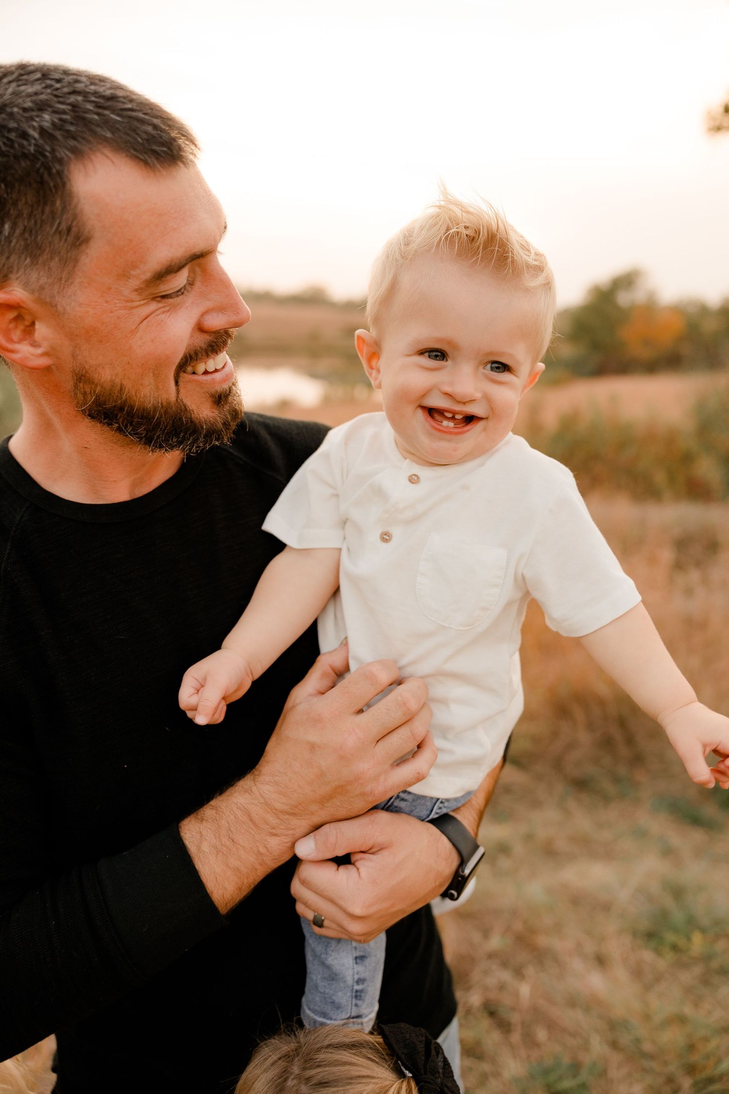 A joyful family moment captured during golden hour in a grassy field outdoors.