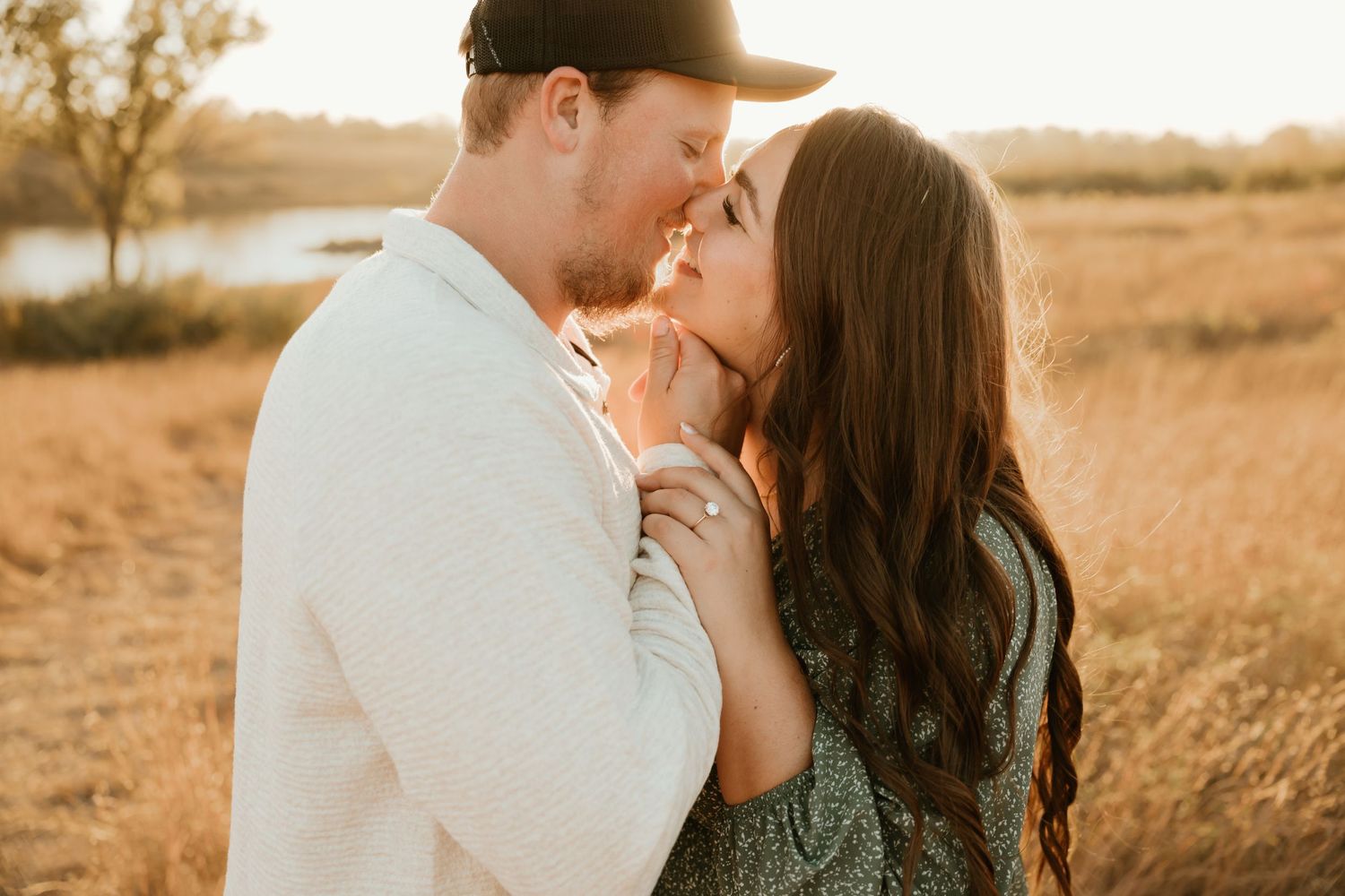 Romantic couple embracing in golden field at sunset near a lake with warm autumn lighting.