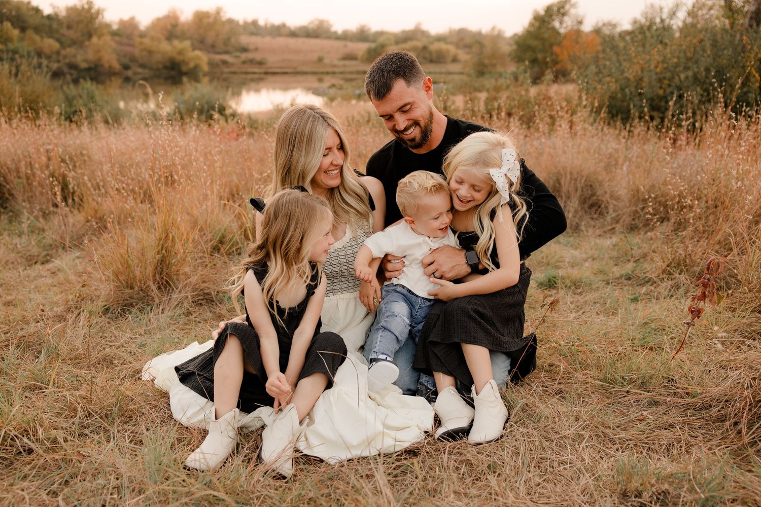 A loving family sits together in a golden autumn field at sunset wearing coordinated black and white outfits.