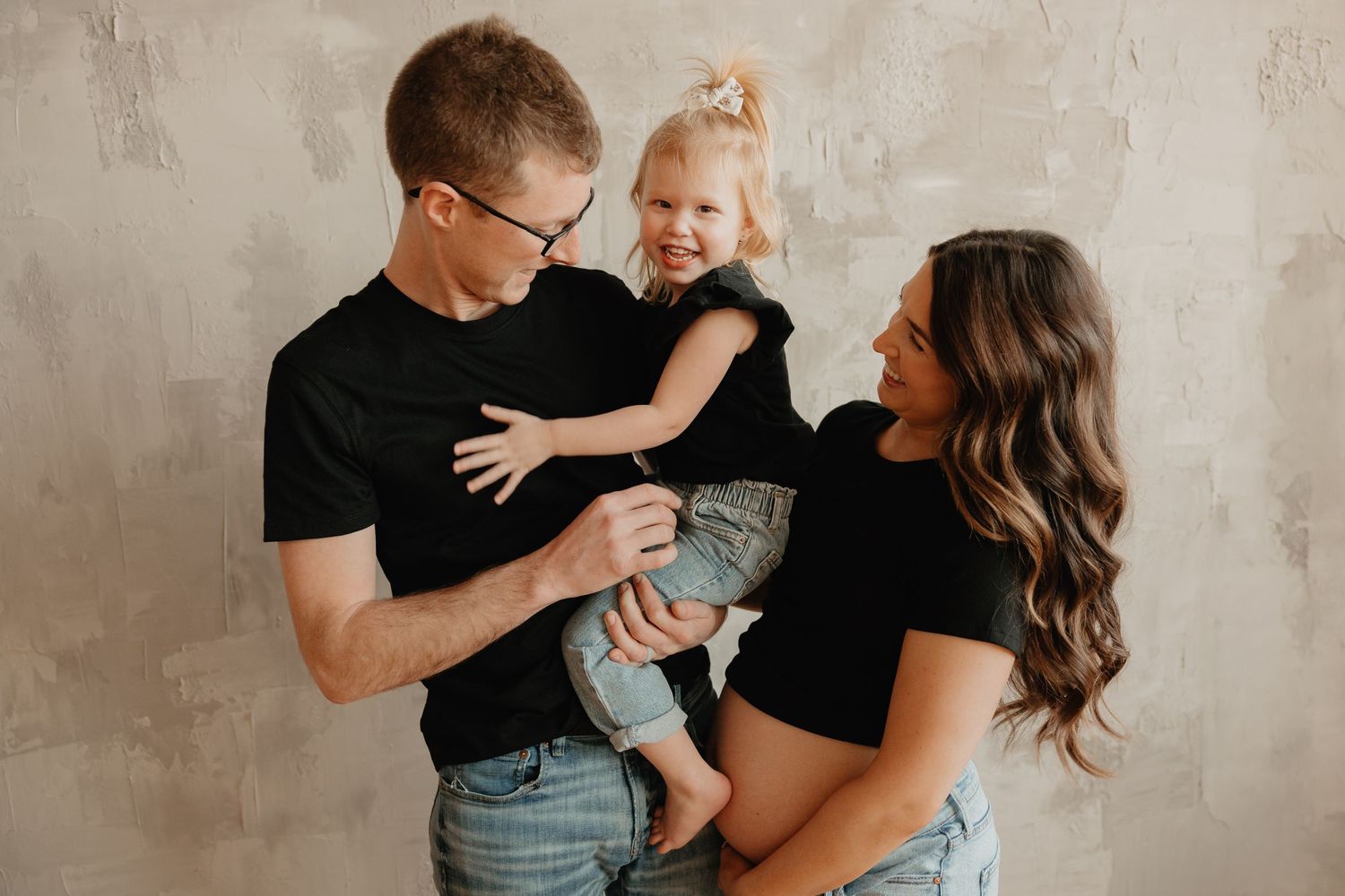 Happy family wearing matching black shirts share a candid moment against textured wall.