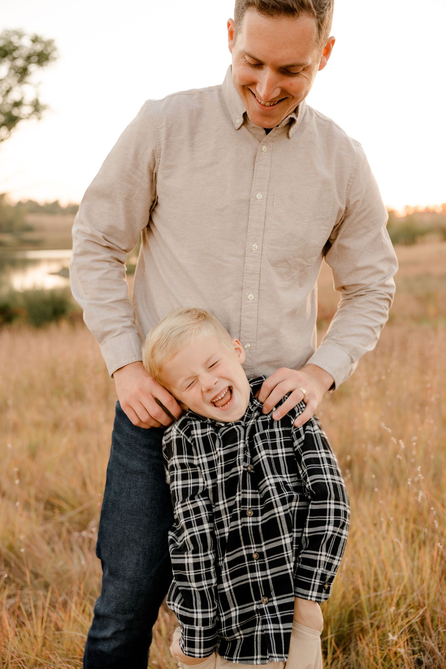 A father and son share a joyful candid moment playing together in a sunlit autumn field.