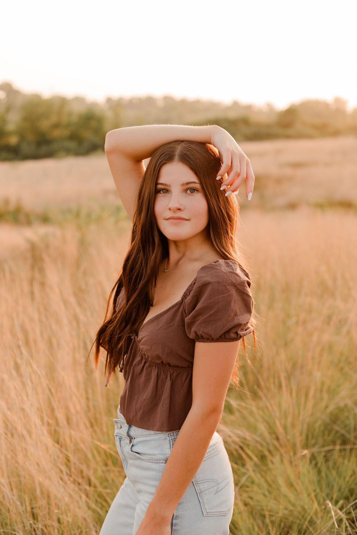 Portrait in field of amber grass at golden hour wearing brown crop top and light denim jeans.