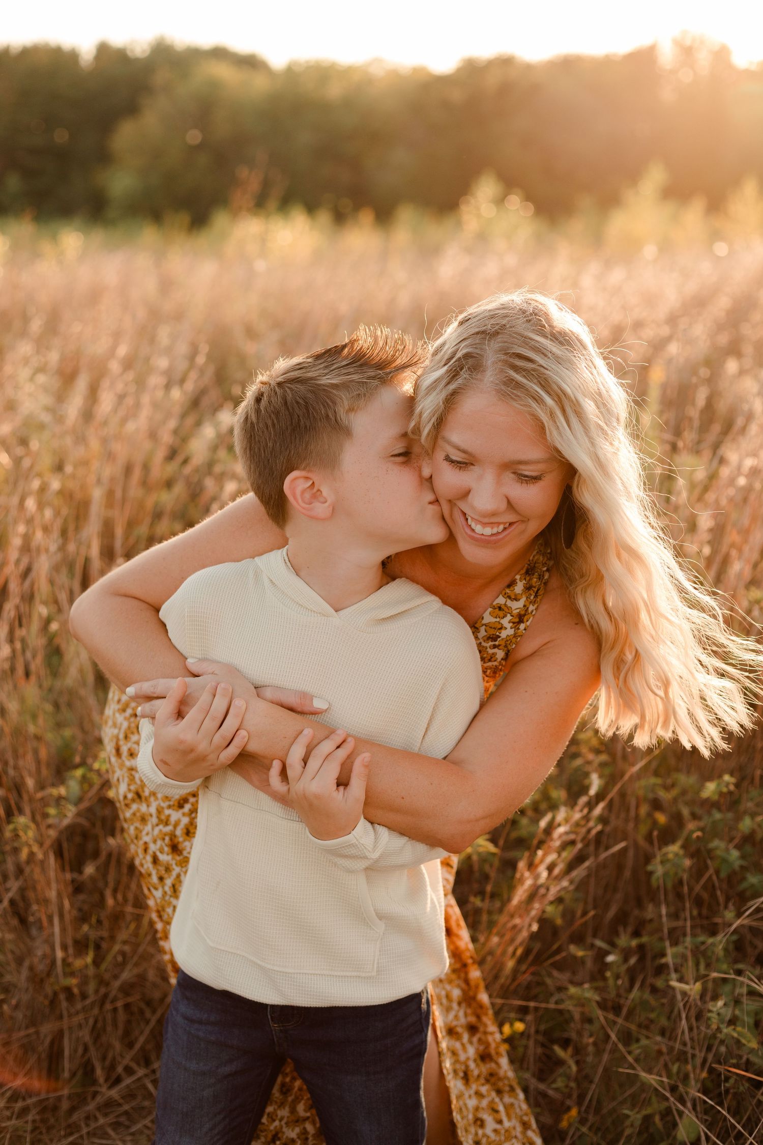 A tender embrace between mother and son in a golden sunlit field at sunset.