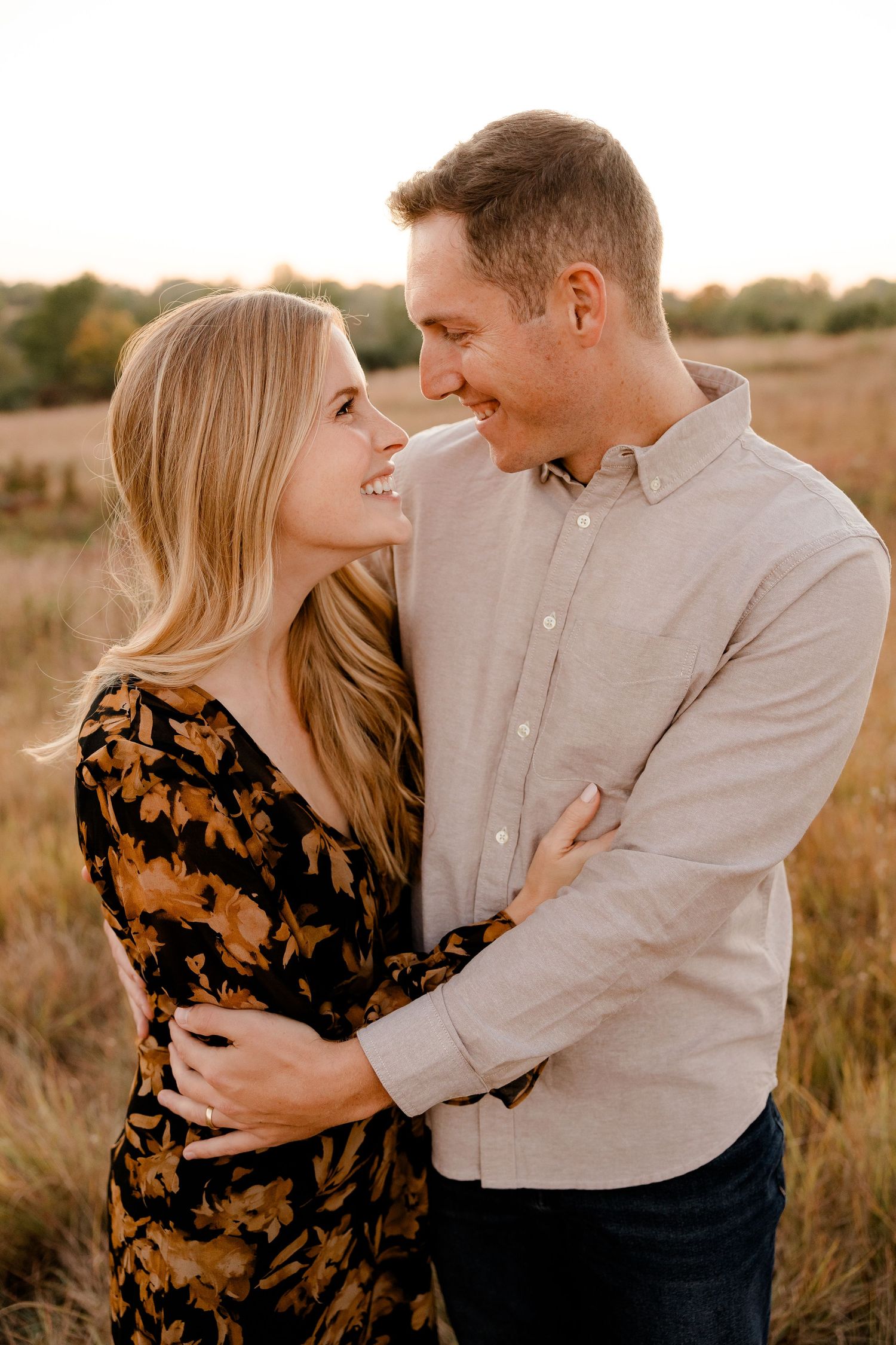 A romantic couple embraces in a golden field during sunset while wearing casual autumn attire.