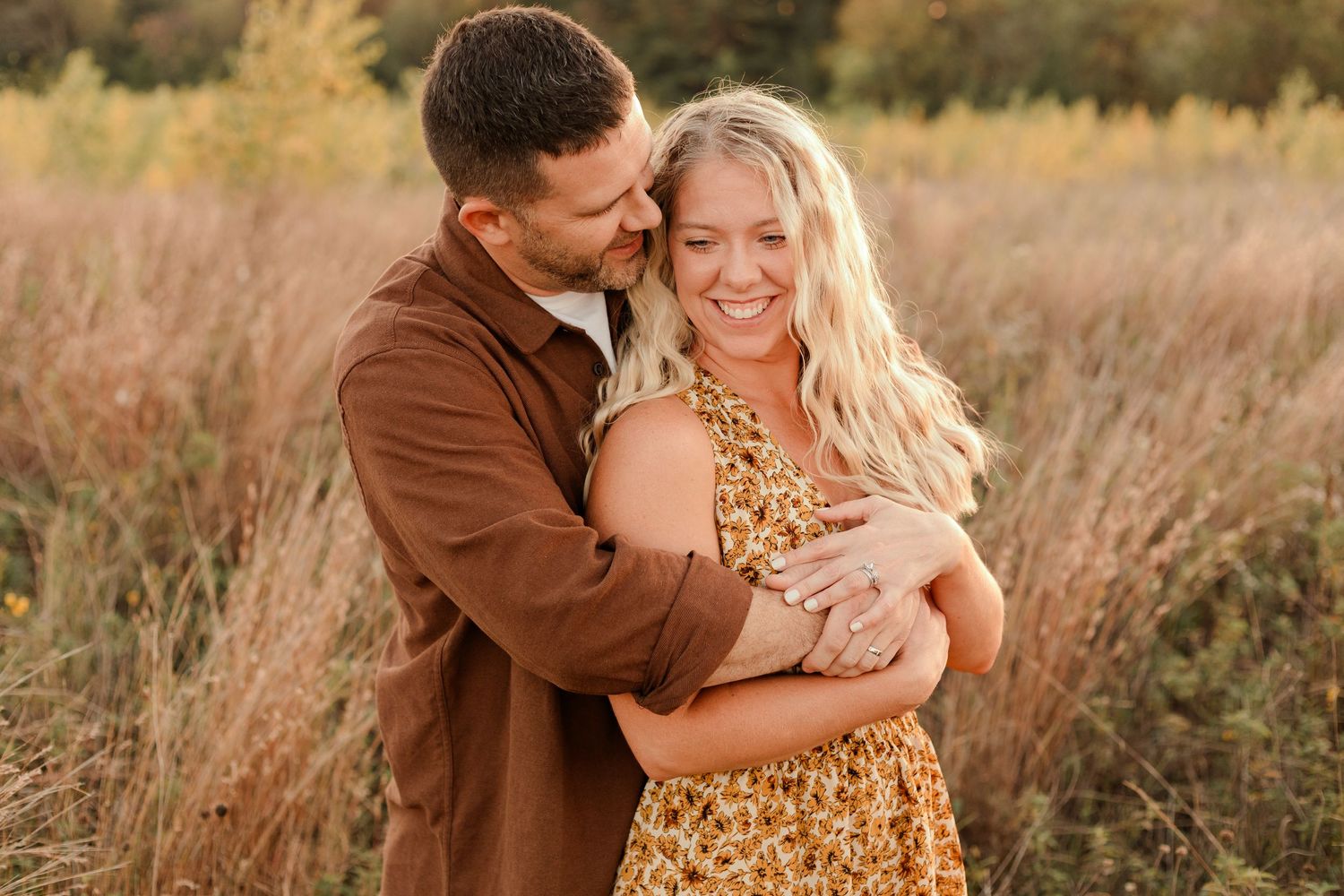 Romantic couple embraces while laughing in a golden field of tall grass during sunset.