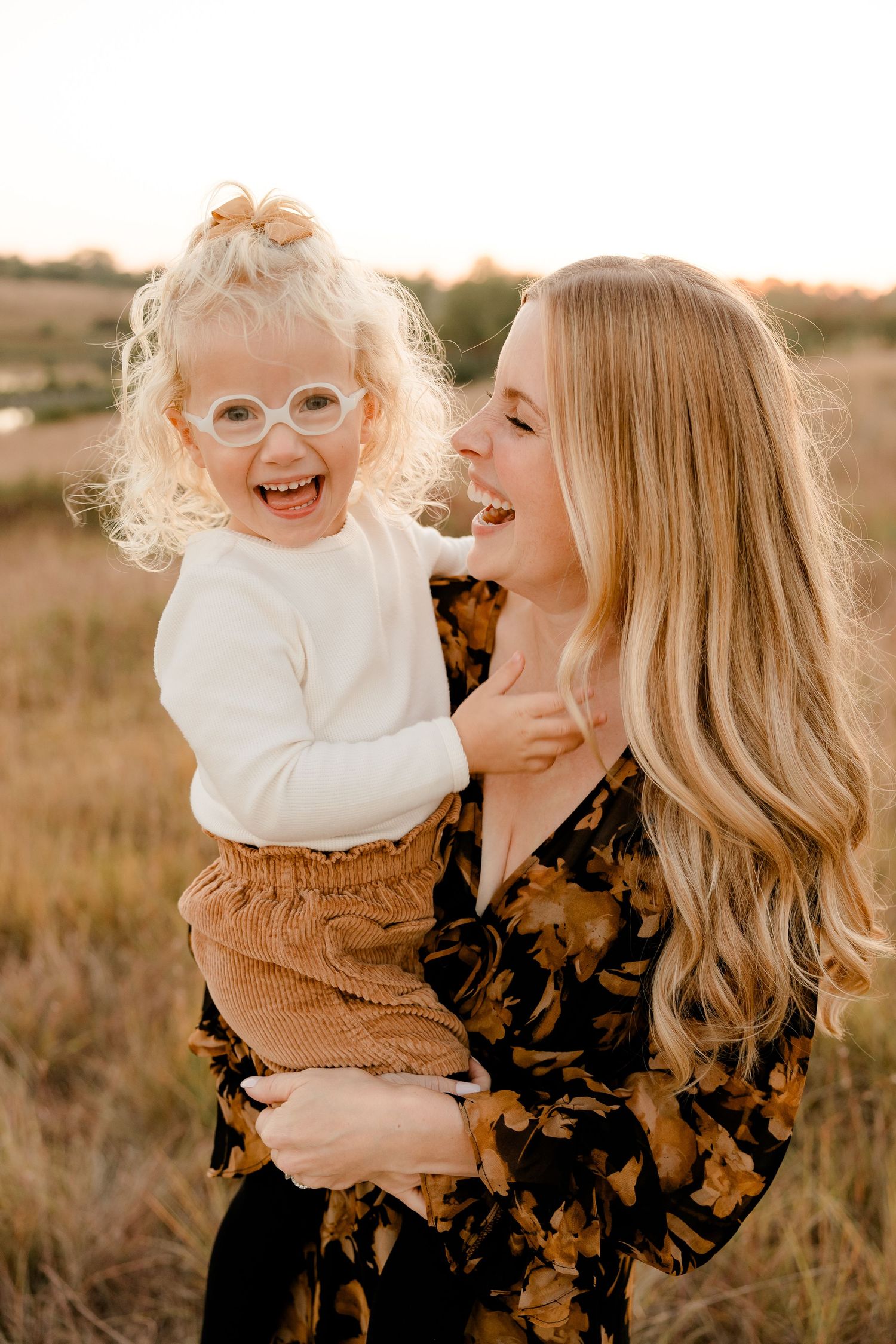 A joyful moment captured at sunset in a field with a floral dress and white sweater against golden light.