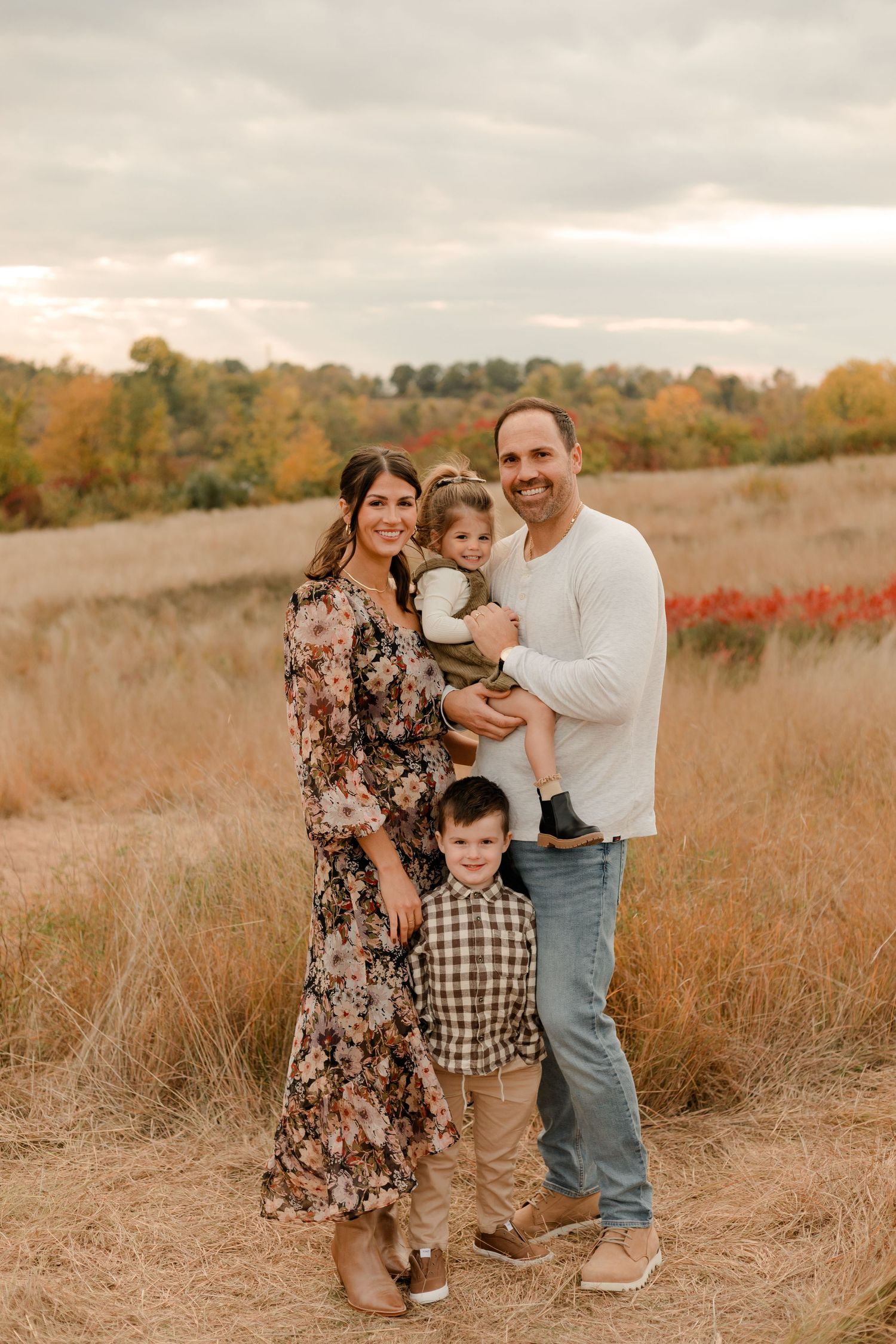 A family poses together in a golden autumn field with tall grass and fall foliage in the background.