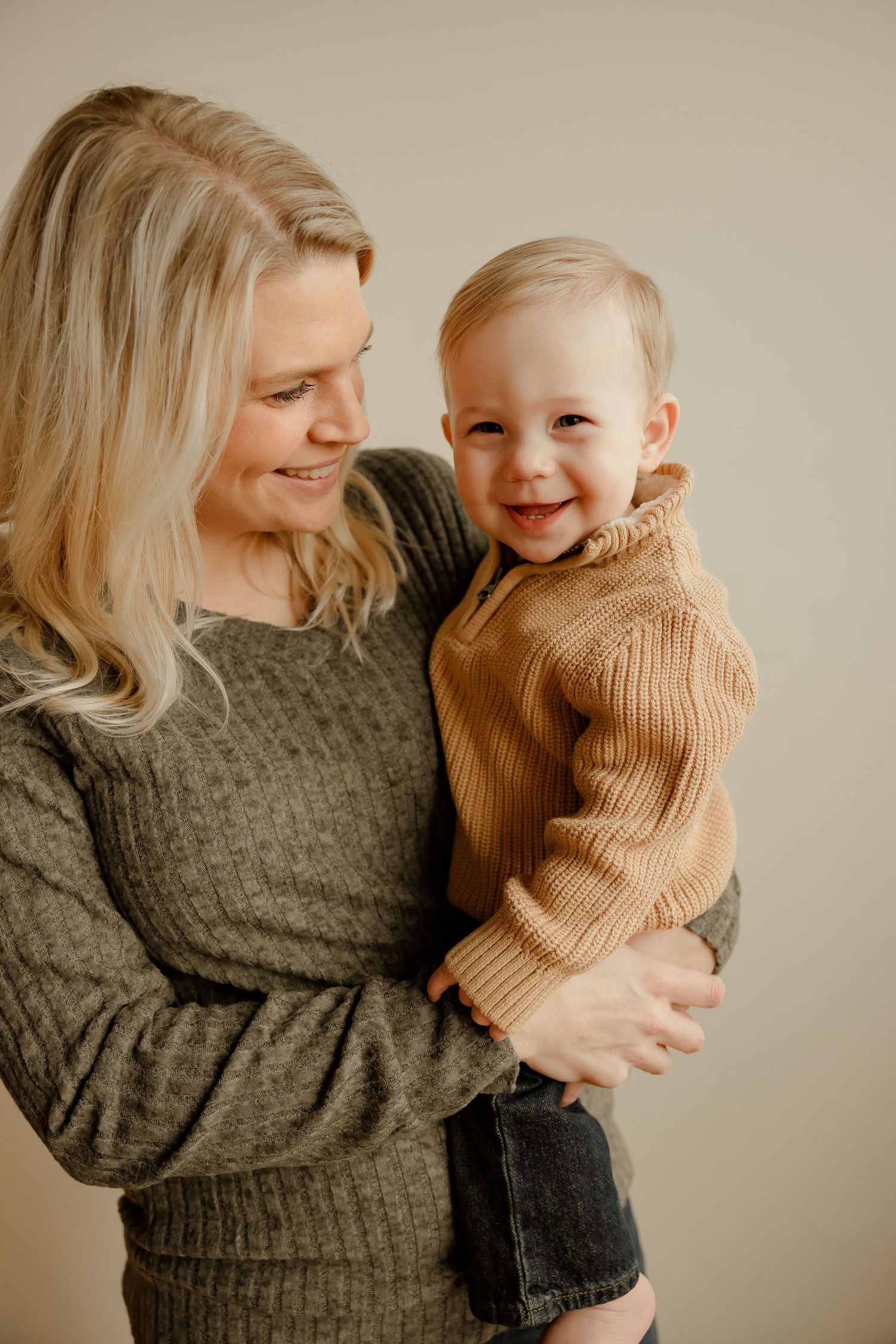 A tender moment captured of a parent and small child wearing cozy knit sweaters against a neutral backdrop.