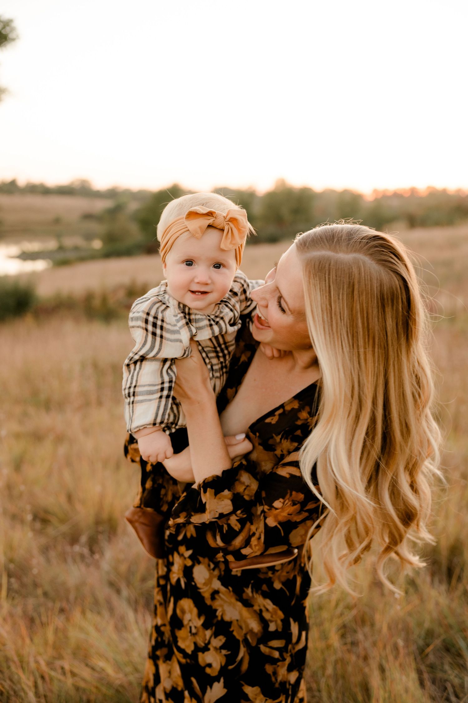 A tender outdoor portrait in a golden field at sunset shows a loving embrace between mother and daughter in autumn attire.