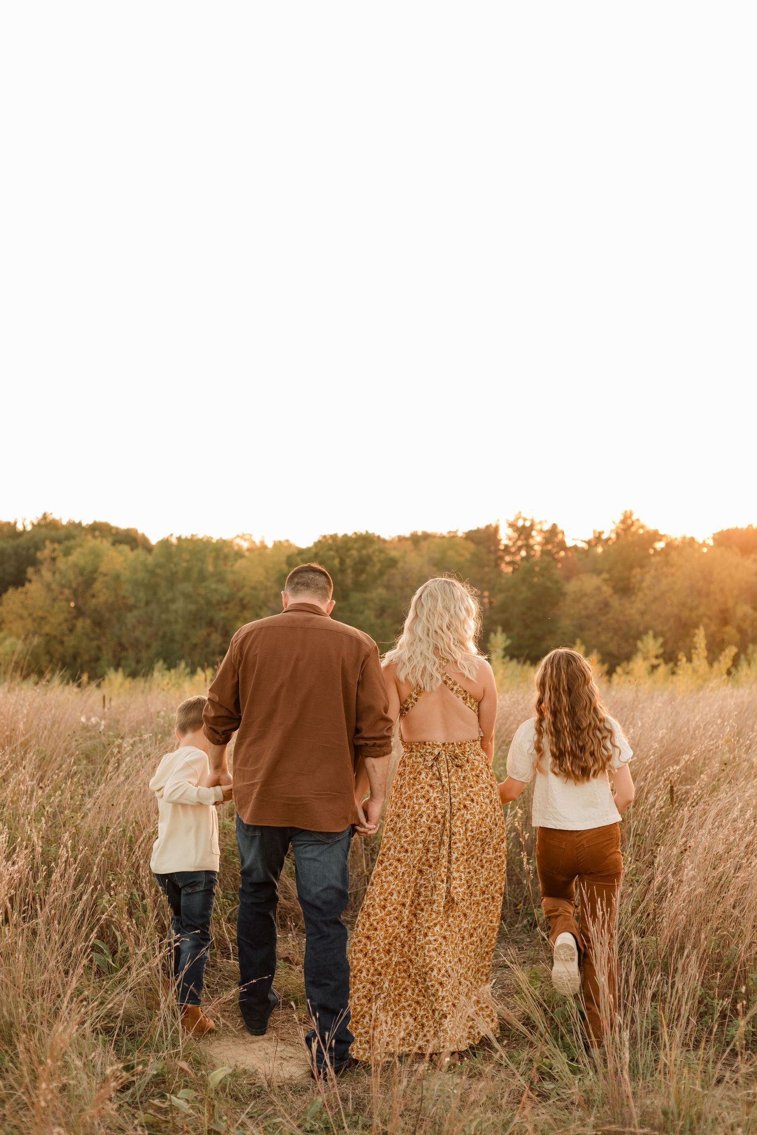Family walks together through tall golden grass field at sunset during autumn outdoor photo session.