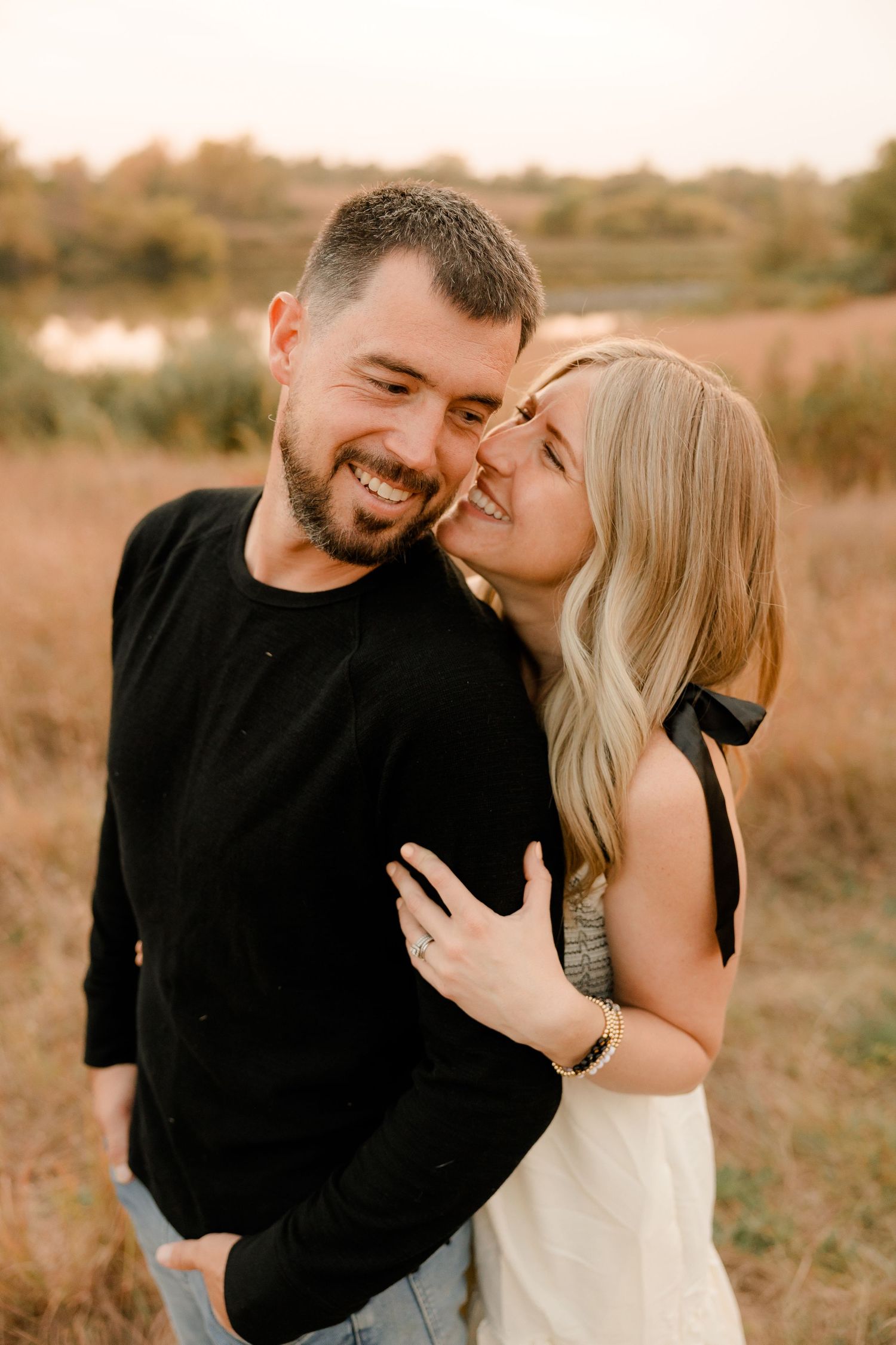 A couple share an intimate moment laughing together in a golden field at sunset.