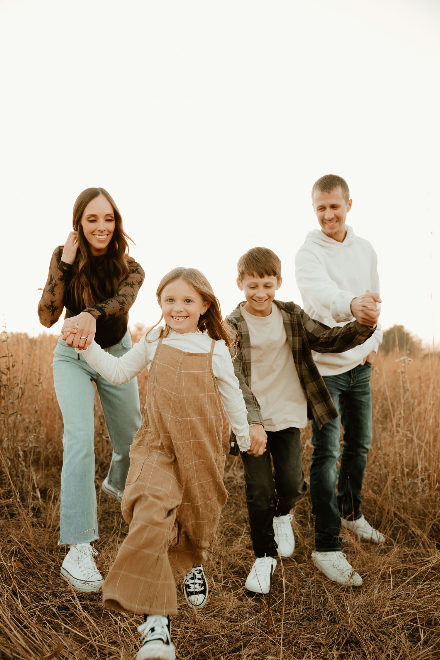 A family walks together through a golden field at sunset wearing casual clothing and sneakers.