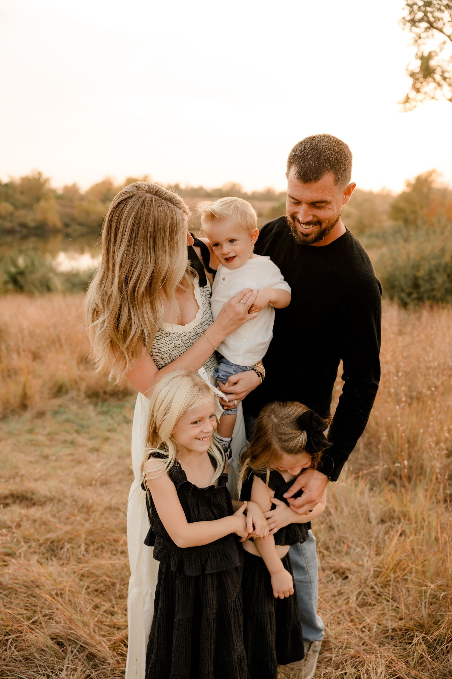 A family shares a joyful moment together in a golden field during sunset, wearing coordinated casual outfits.