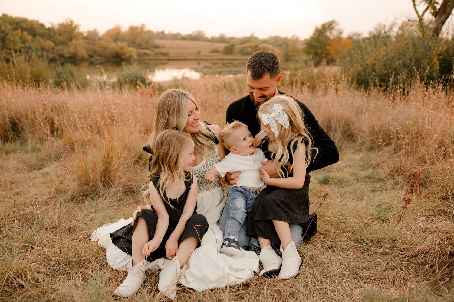 Family sitting in golden field at sunset sharing tender moment together in nature.