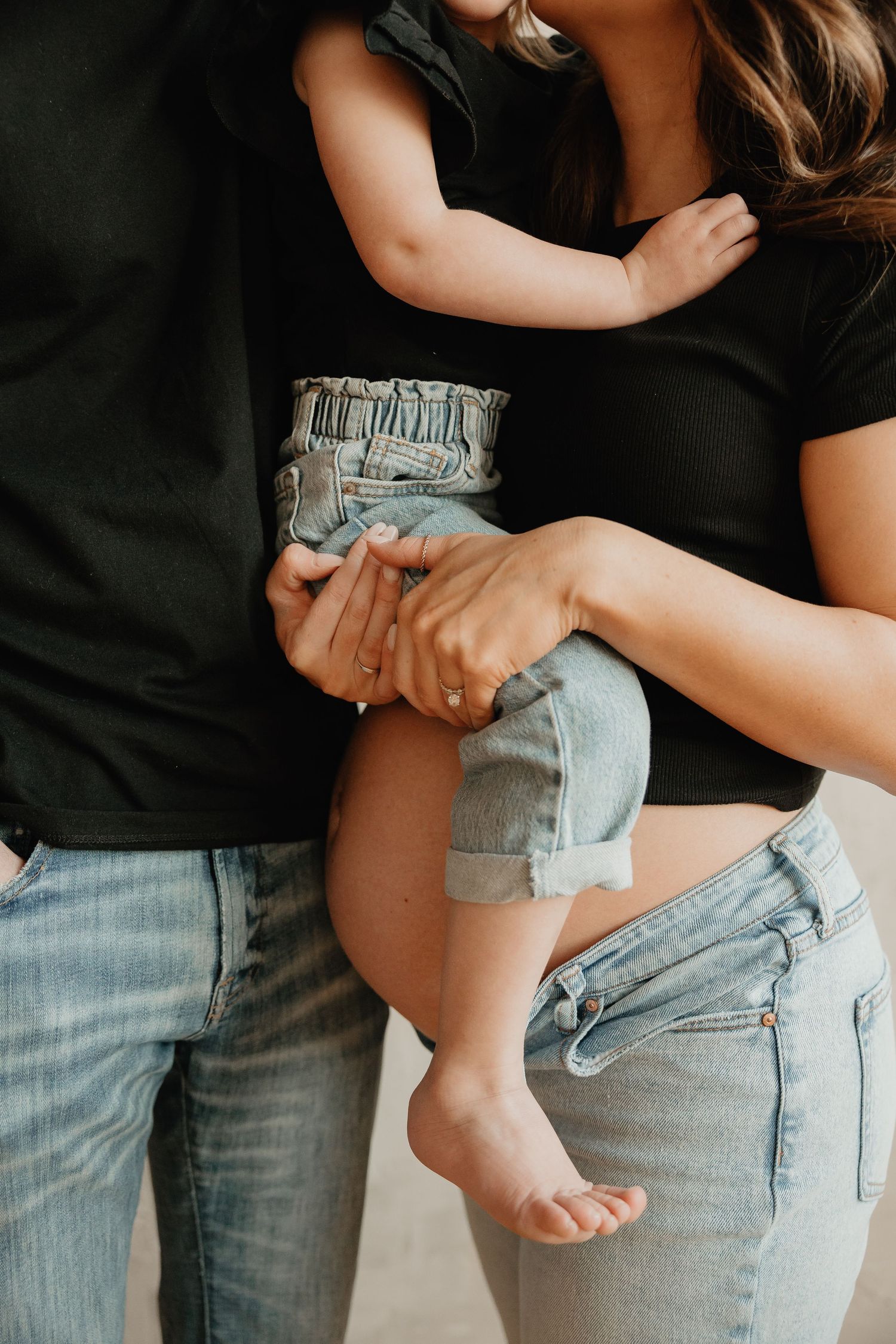Close-up view of a baby's bare feet and legs being held while wearing denim shorts against dark background.