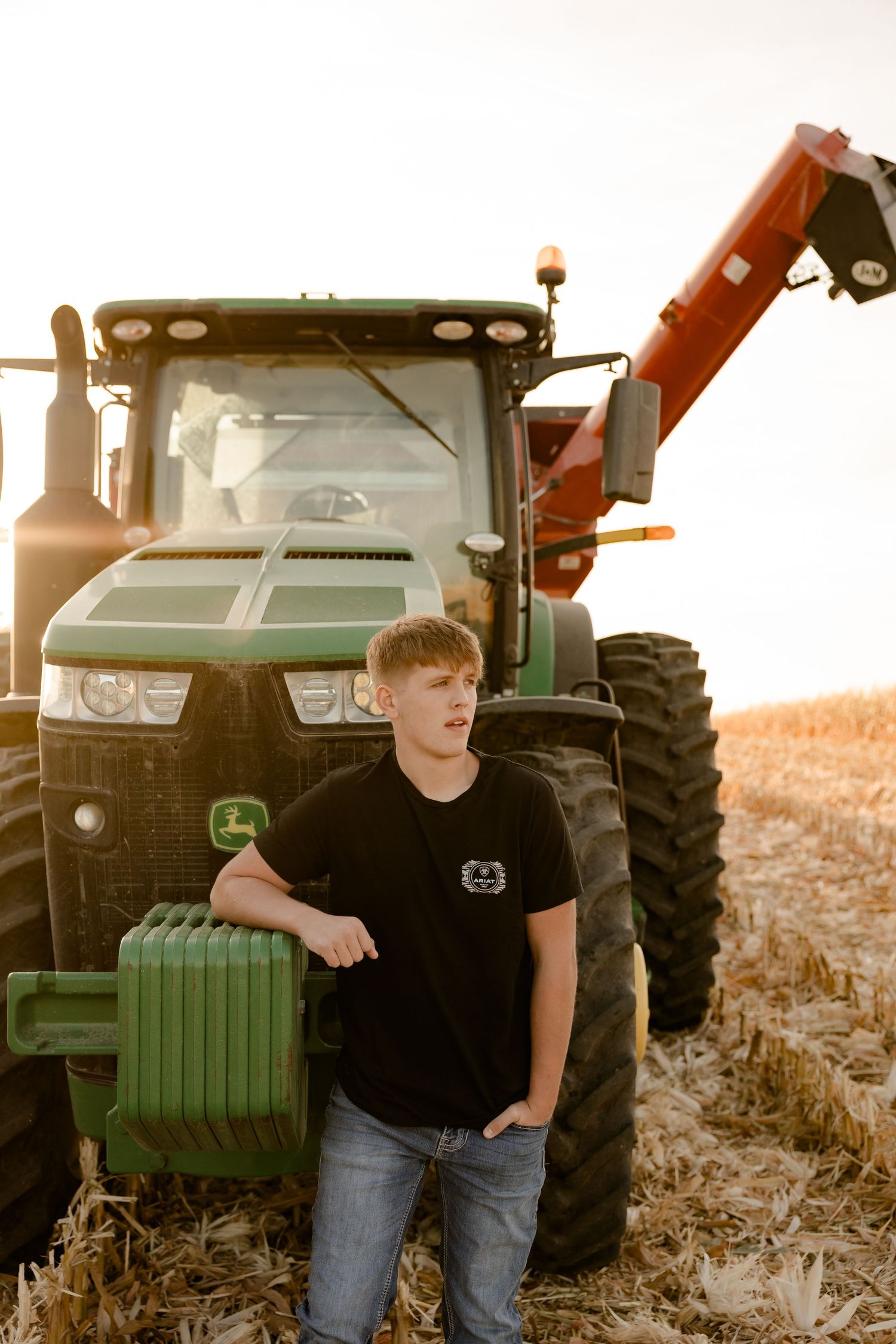 A large green John Deere tractor stands in a harvested field during golden hour.