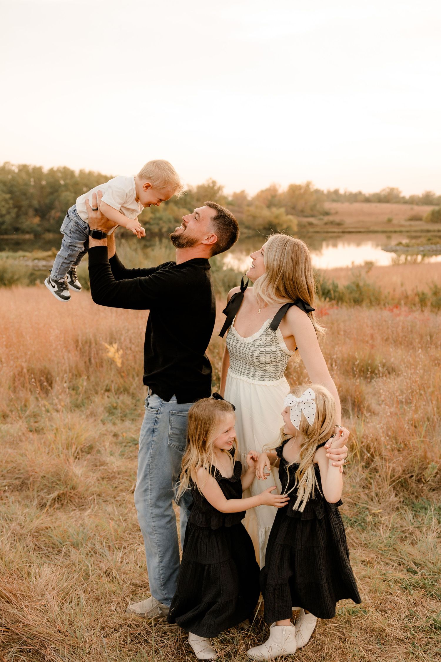 A family shares a joyful moment together in a golden field at sunset near a pond during an outdoor photo session.