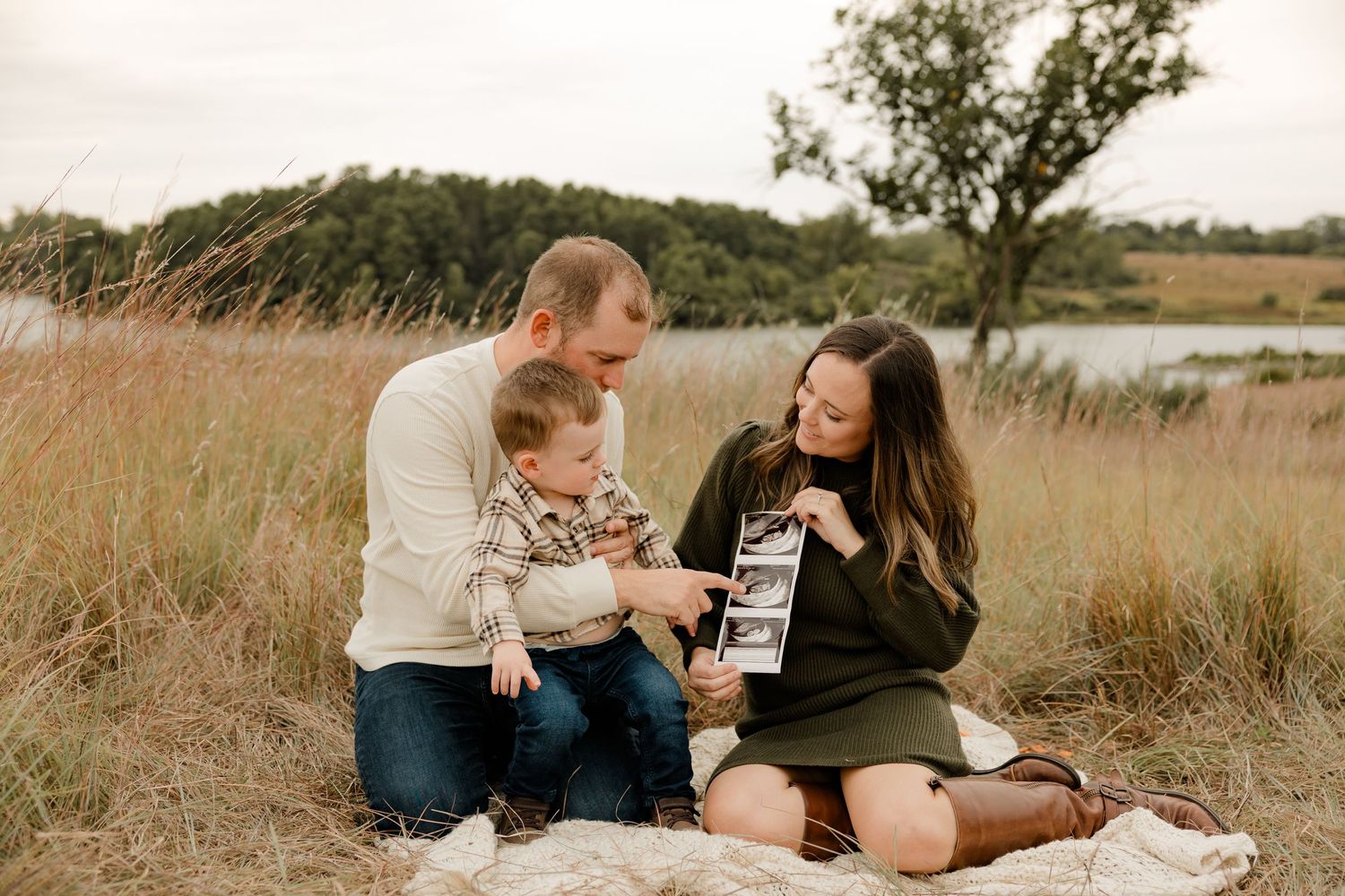 Family sitting on blanket in grassy field near water enjoying warm sunset together.