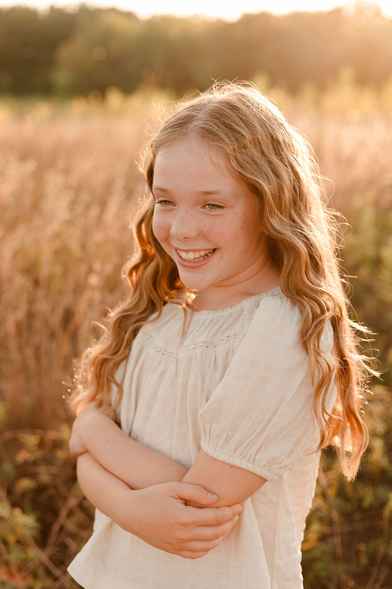 A young girl in a white top laughs joyfully in a golden field at sunset.