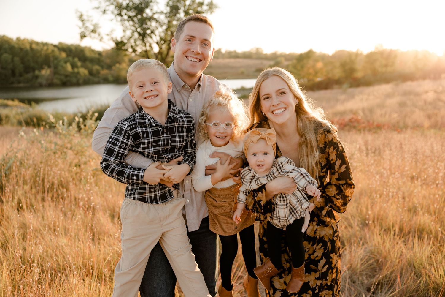 A family stands together in a golden field at sunset near a lake on an autumn evening.