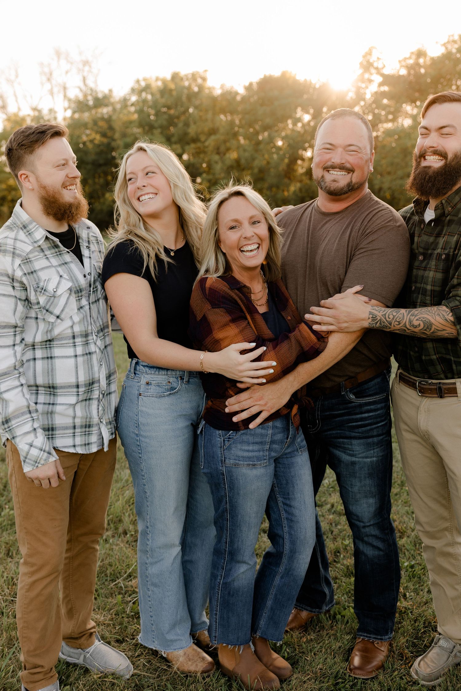 A family laughing together outdoors at sunset while wearing casual clothing.