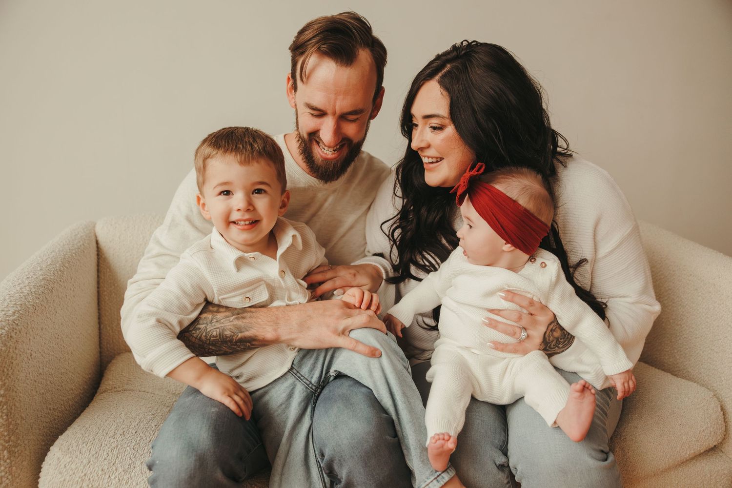 Family in white sweaters sitting together on beige couch sharing intimate moment in the studio.
