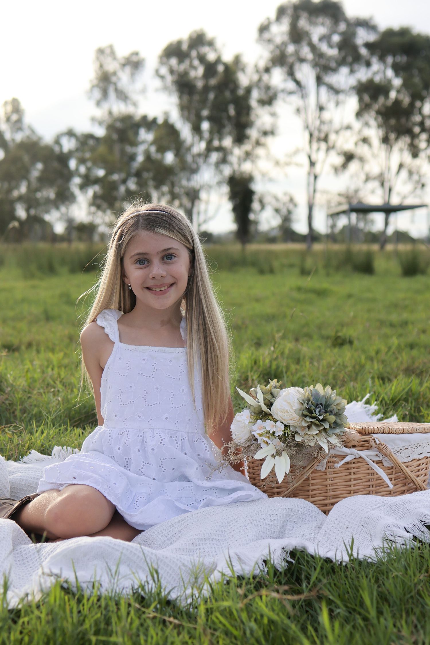 Country picnic scene with white blanket and wicker basket in grassy field.