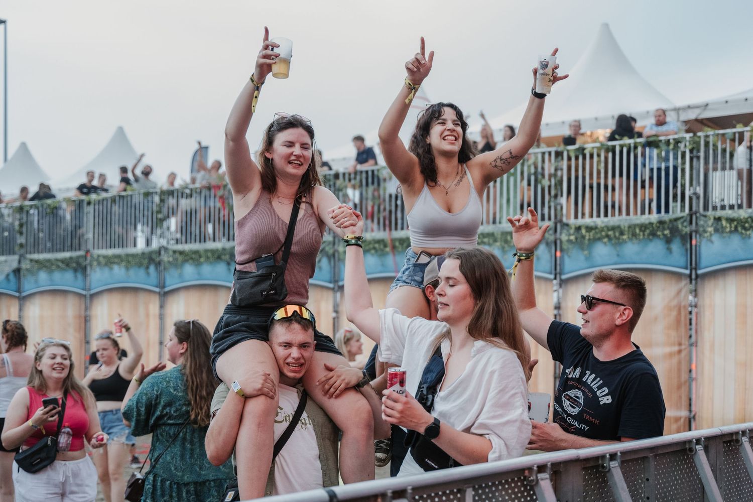 Twee meisjes die op de schouders zitten van twee jongens op een dance festival met biertjes in de hand
