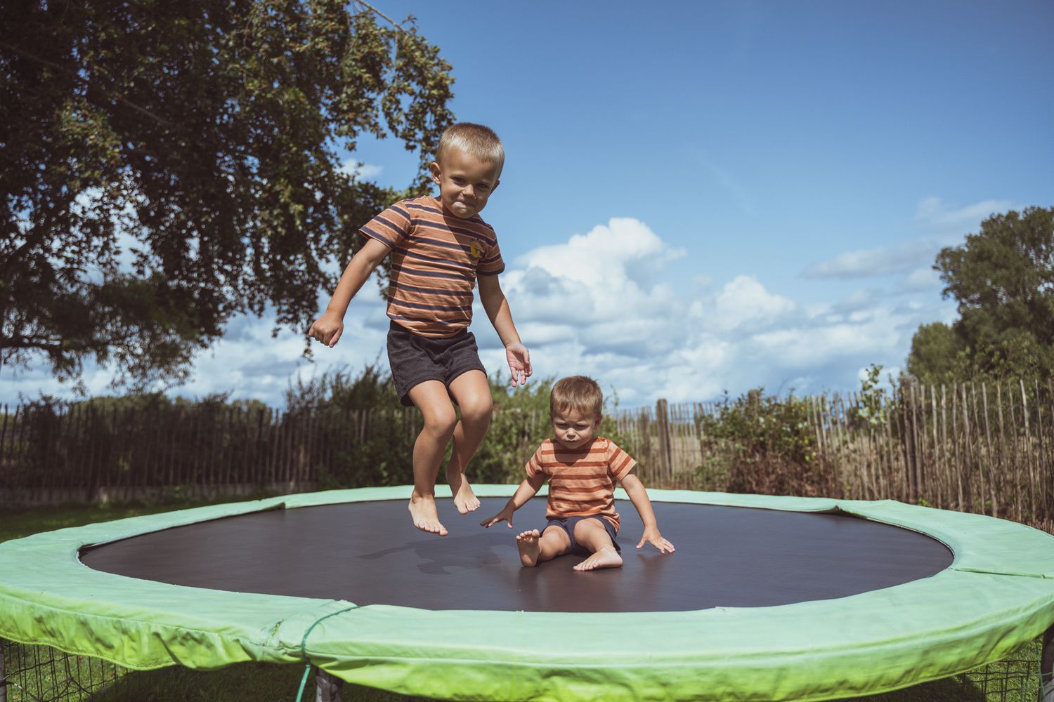 Twee broertjes die op een trampoline springen in een tuin