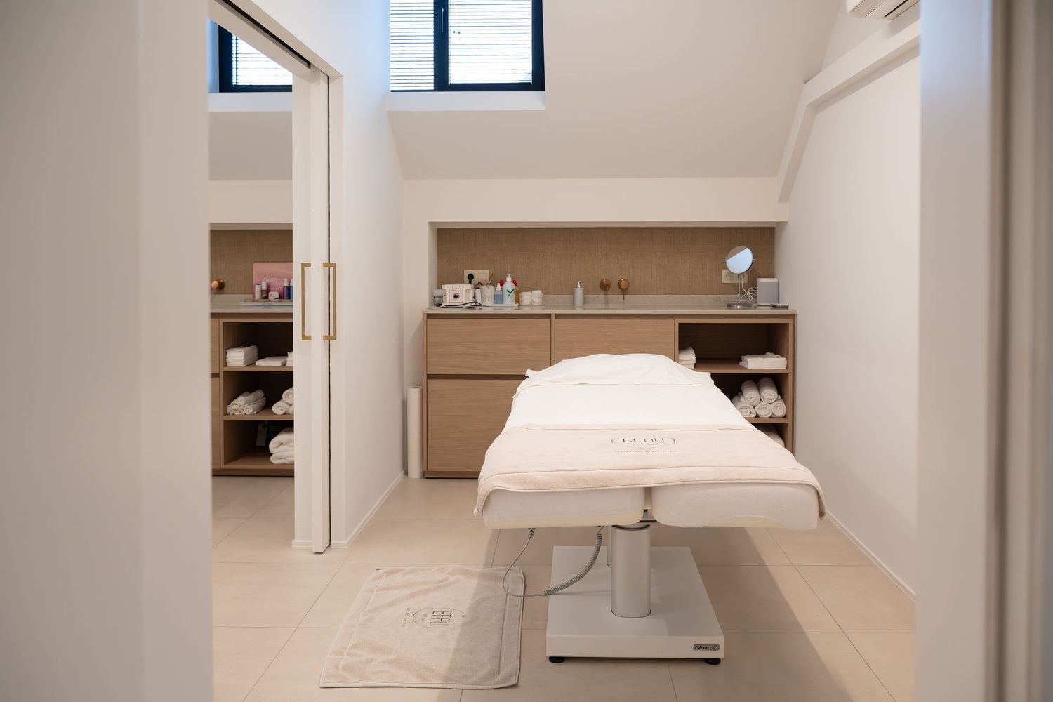 Een kleurenfoto van een zachtkleurig interieur van een schoonheidssalon, waar een behandeltafel staat.