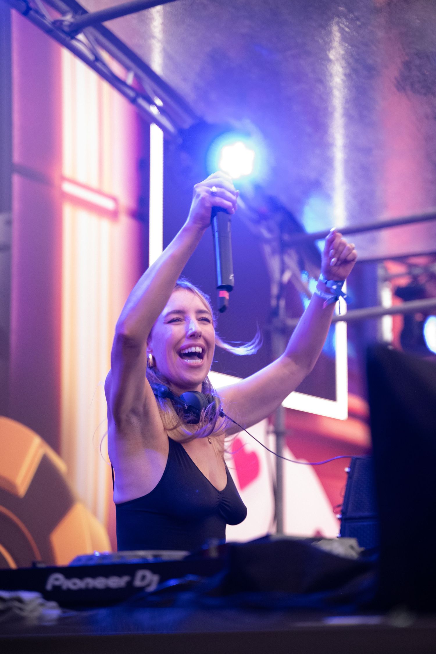 Een gelukkige vrouwelijke DJ die met de handen in de lucht staat