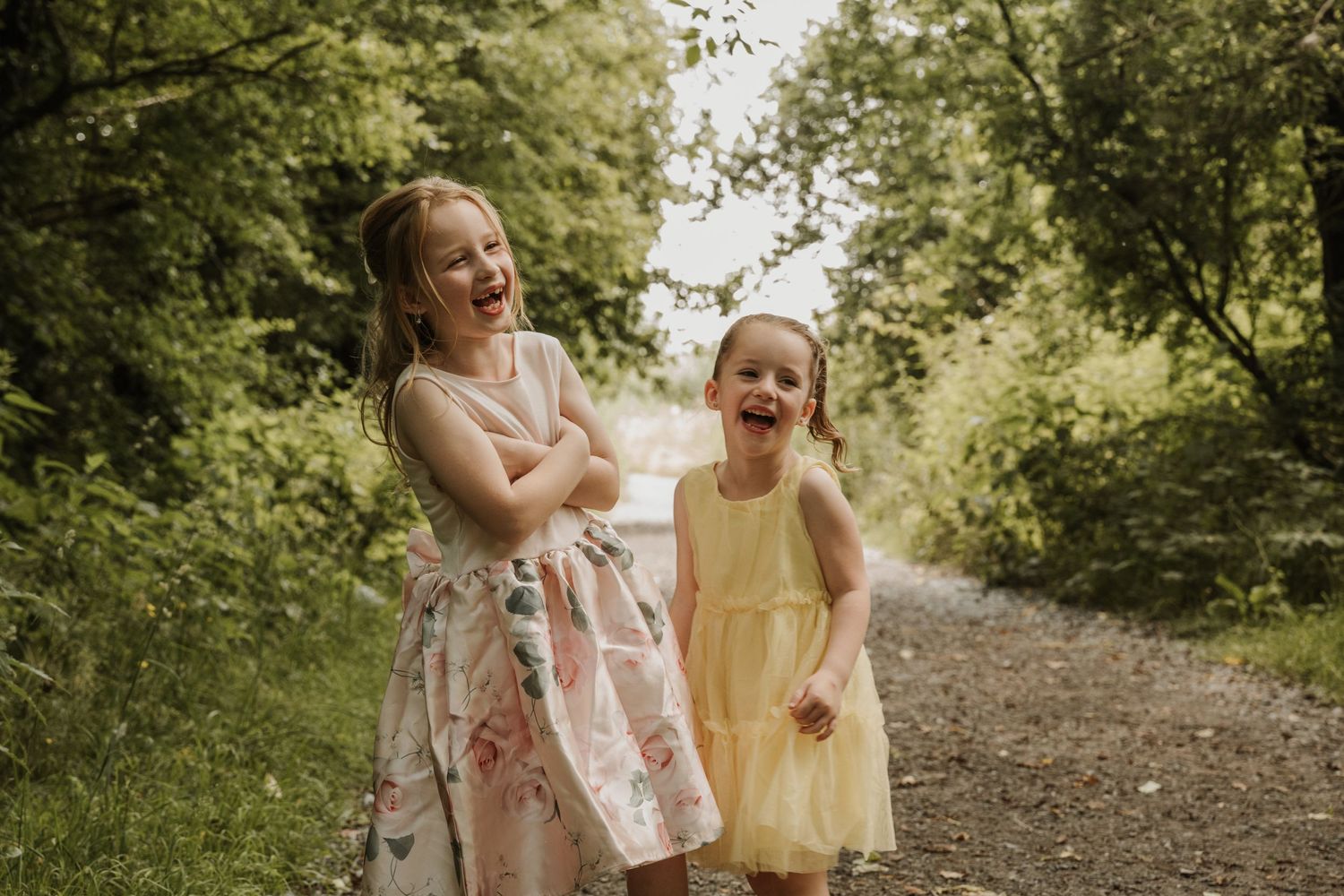 Twee zusjes die lachend op de foto staan in een boomrijke omgeving