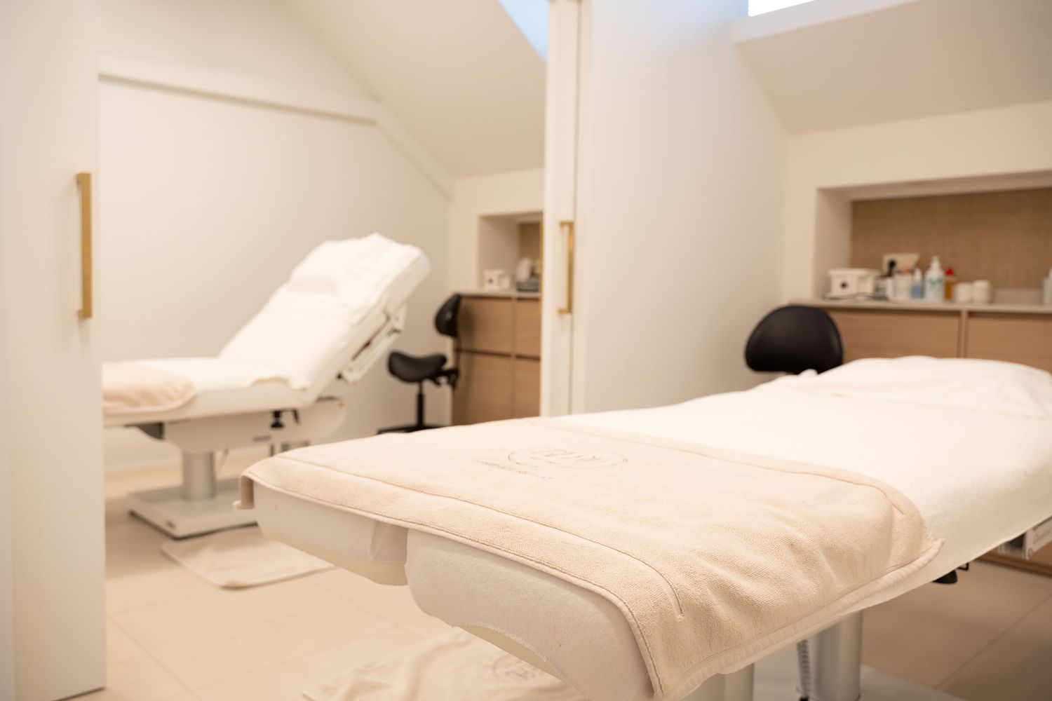 Een kleurenfoto van een zachtkleurig interieur van een schoonheidssalon, waar een behandeltafel staat.