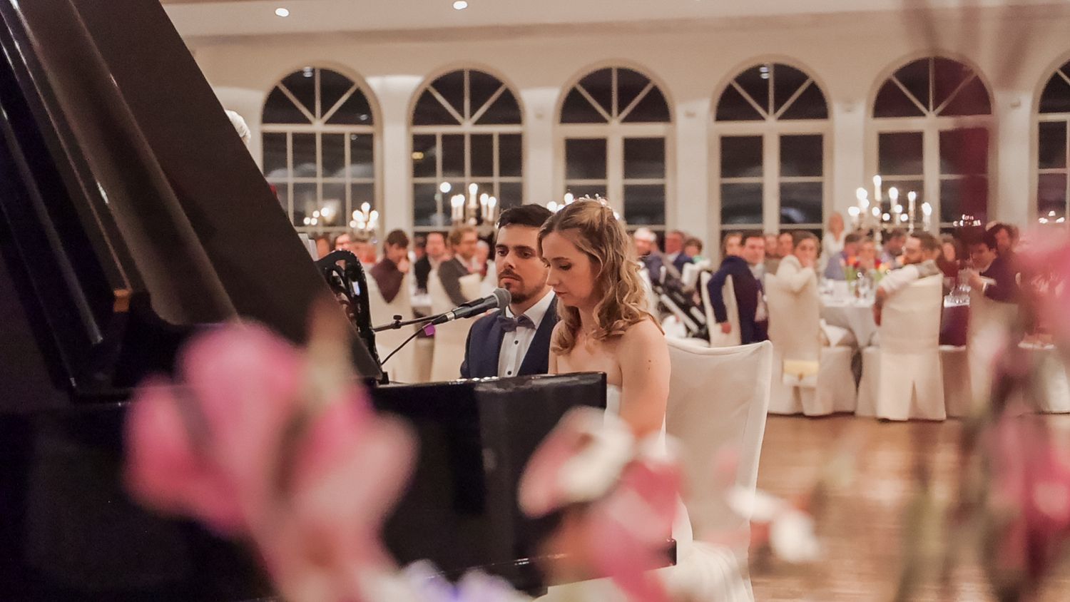 Pas getrouwd koppel dat op de piano een zangstukje brengt tijdens hun huwelijksfeest