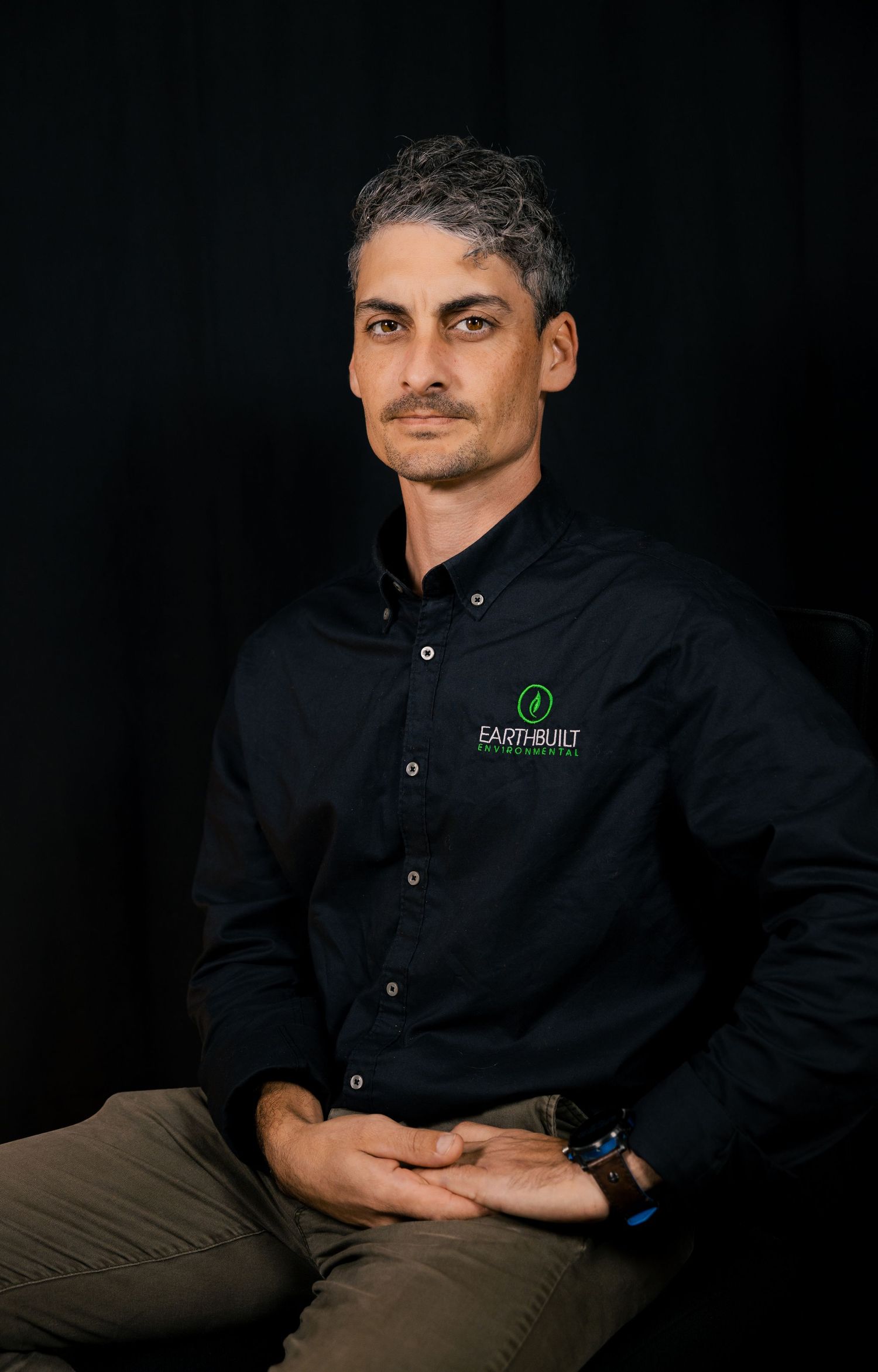 Corporate-style portrait of man in dark shirt, professional headshot.