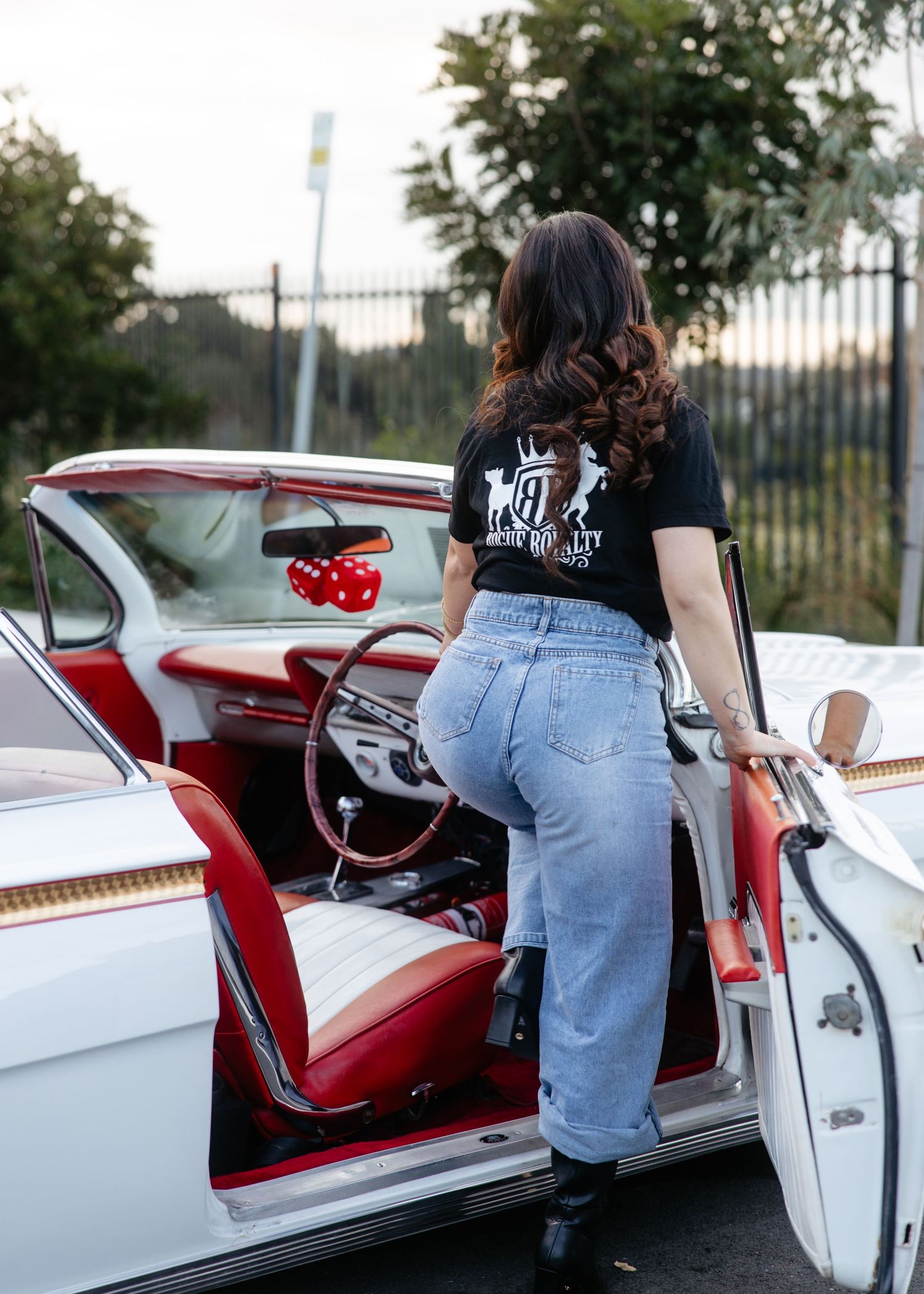 Woman leaning on open car door of white classic car, sunset light.