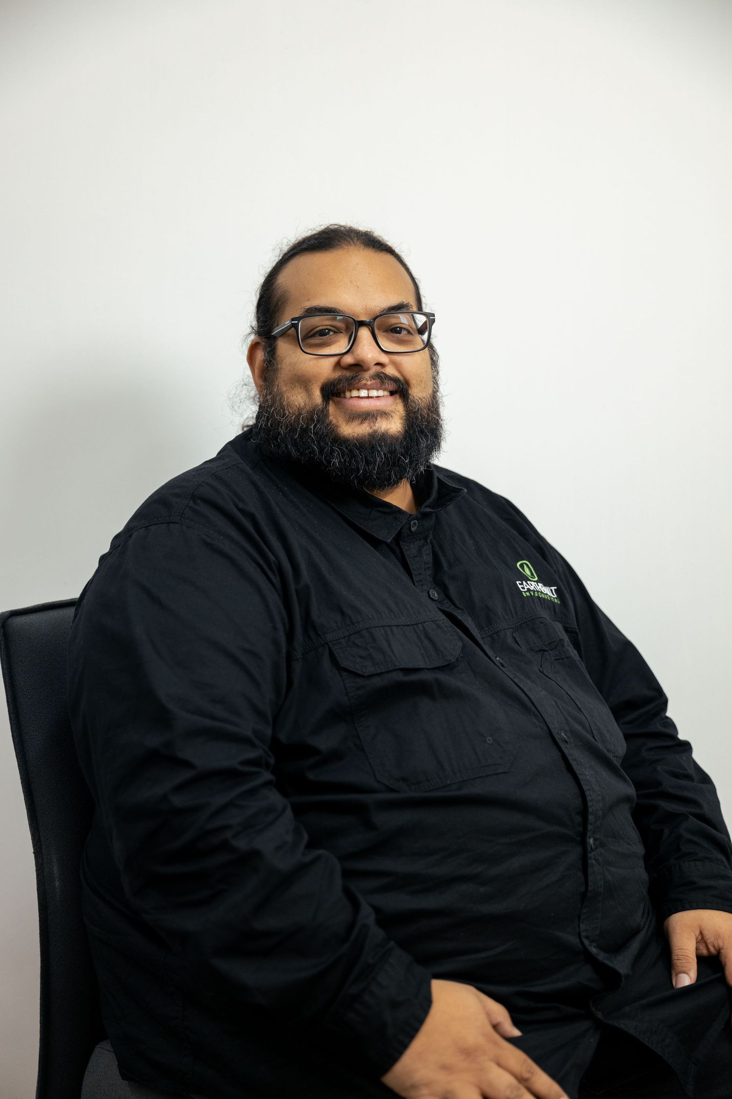 Corporate headshot of man in black shirt, seated against white backdrop.