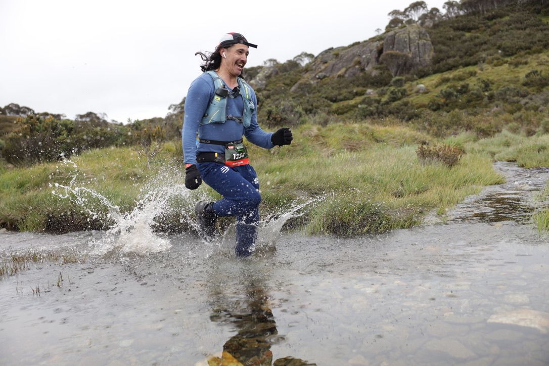 Trail runner splashing through water during endurance race.