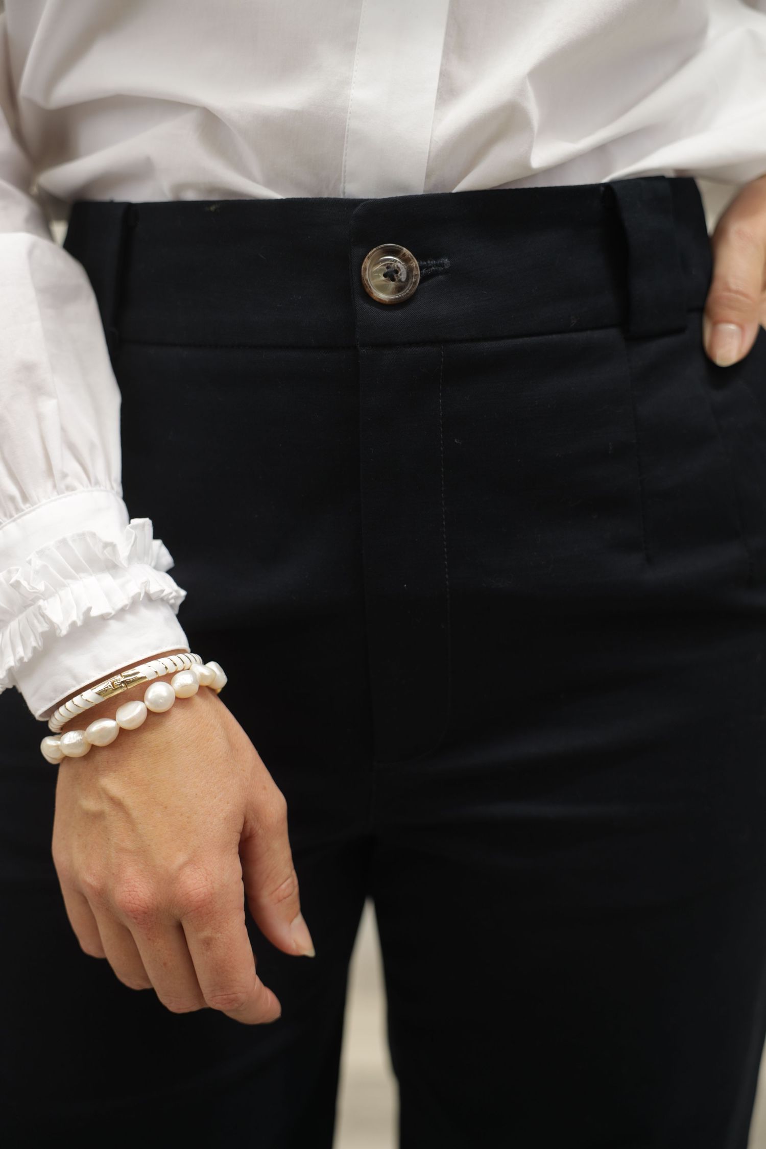 A close-up lifestyle portrait of a female model in black tailored pants paired with a crisp white shirt. The frame captures from the upper t