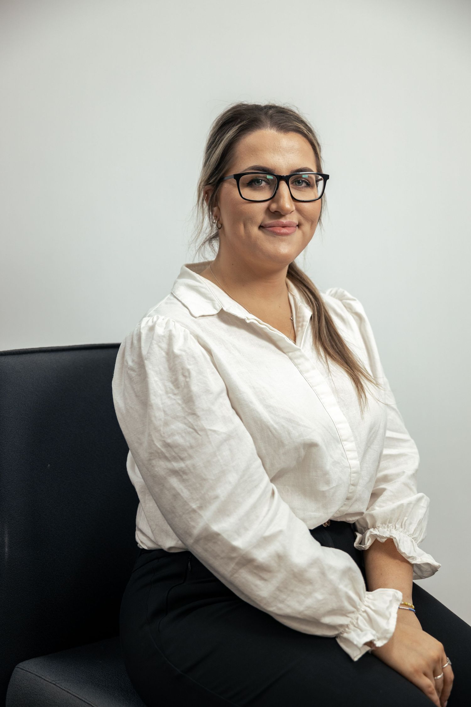 Corporate headshot of woman in glasses and white blouse, seated indoors.