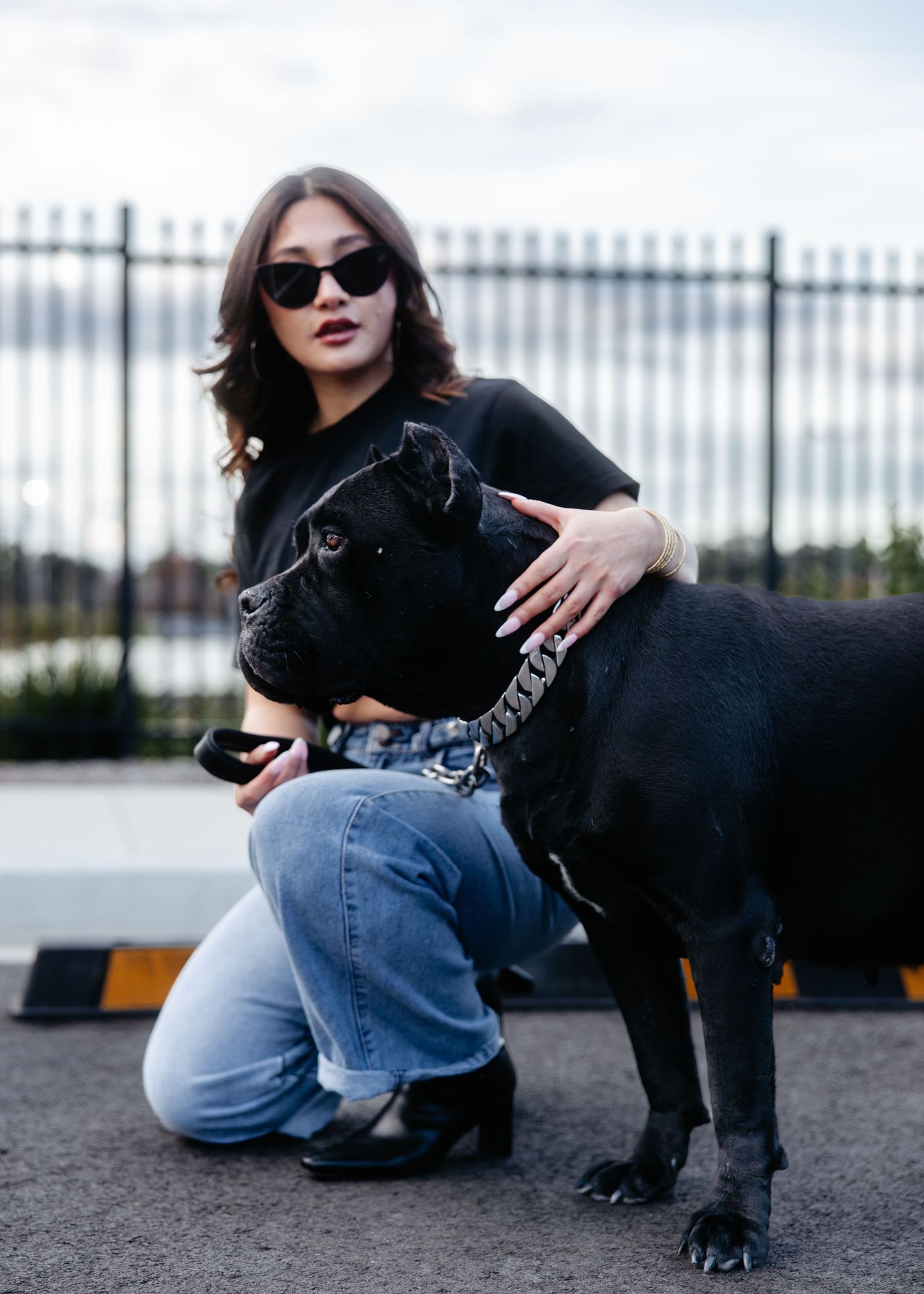 Woman in black outfit posing with dog, outdoor urban scene.