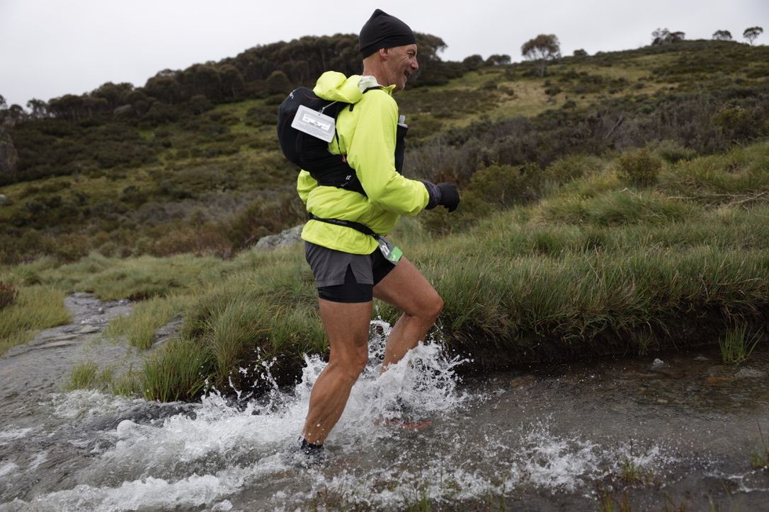 Athlete in neon vest running across rugged outdoor trail.