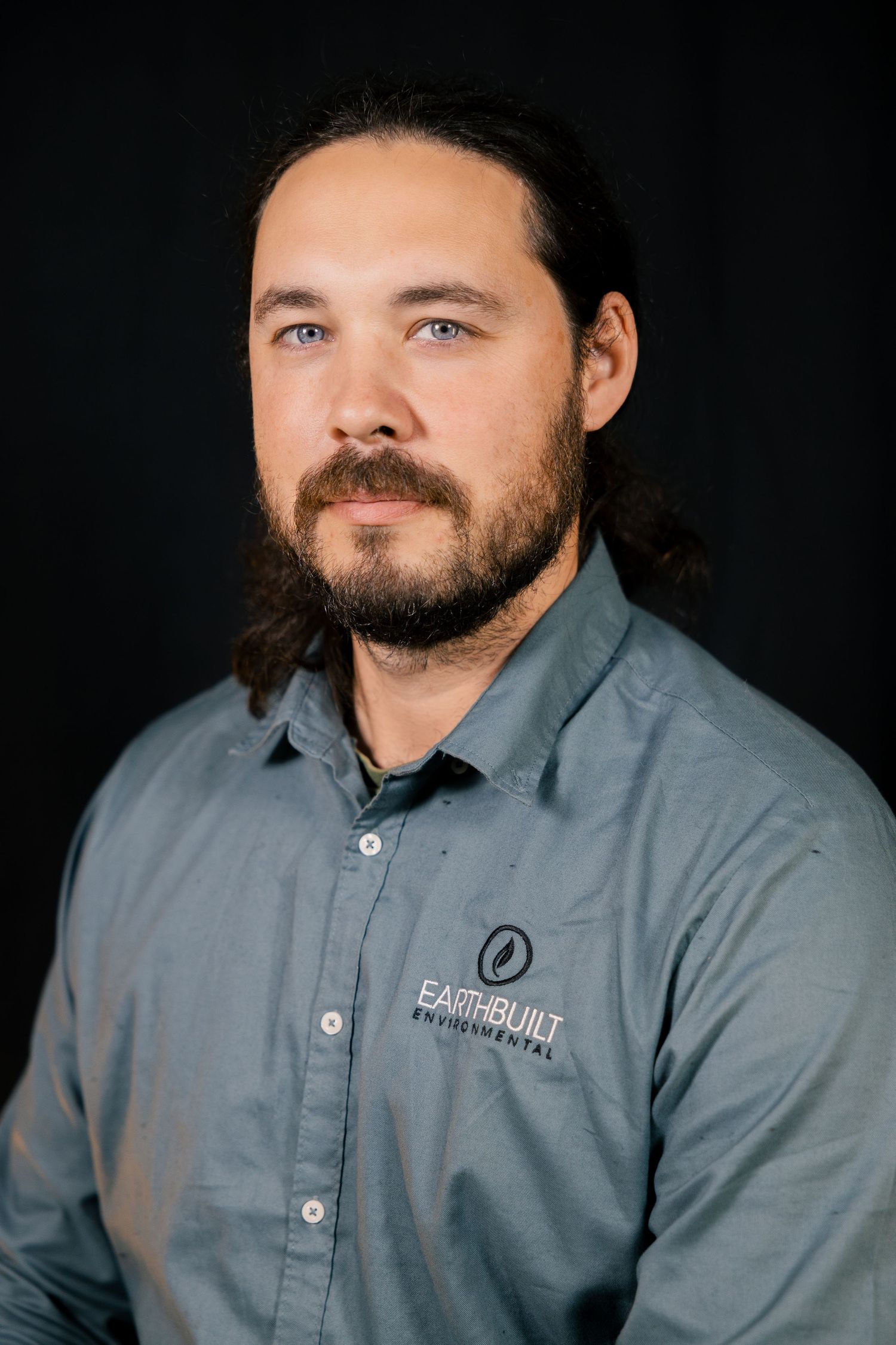 Studio headshot of man in grey shirt, seated corporate portrait.