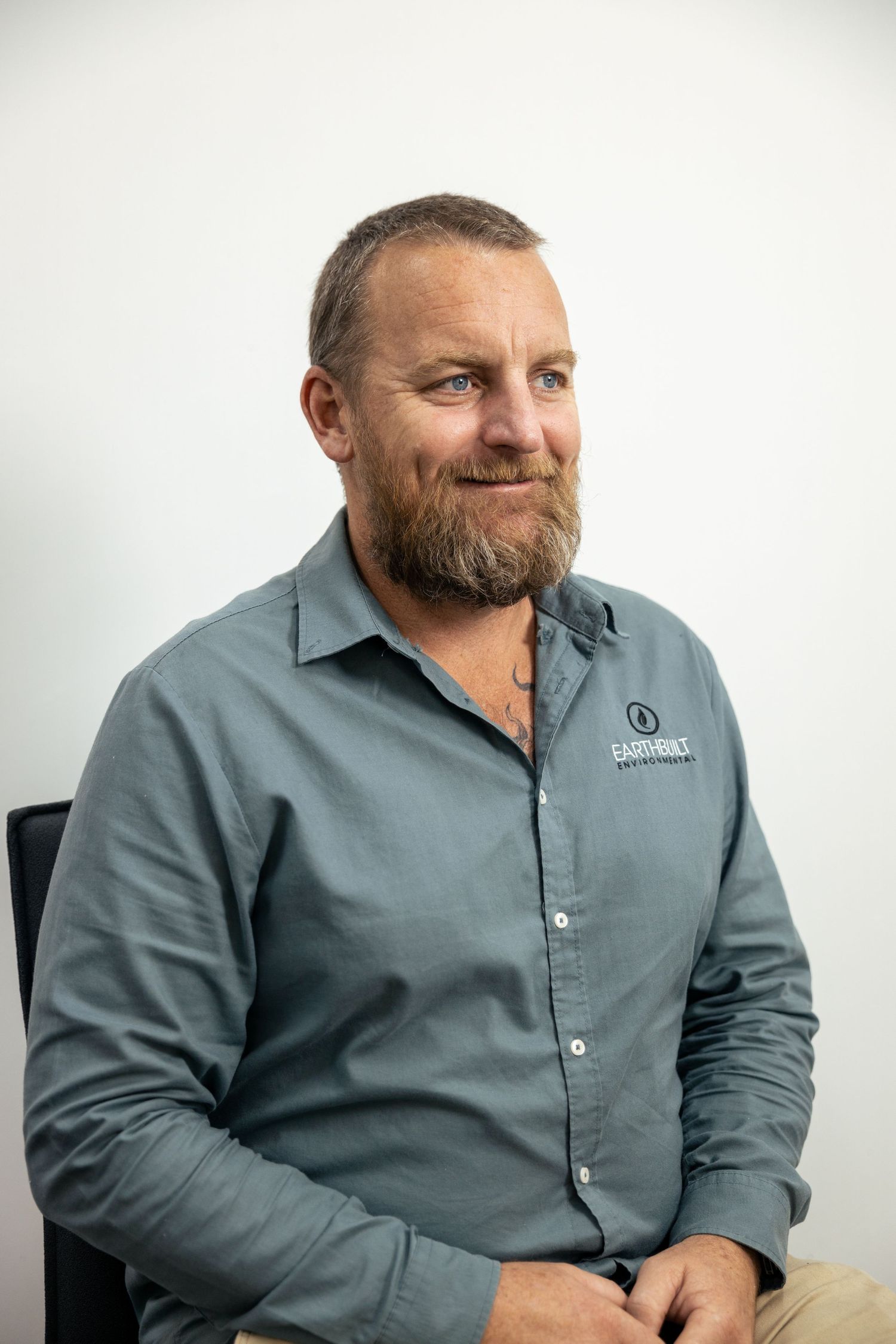 Corporate portrait of man with beard in grey shirt, white backdrop.