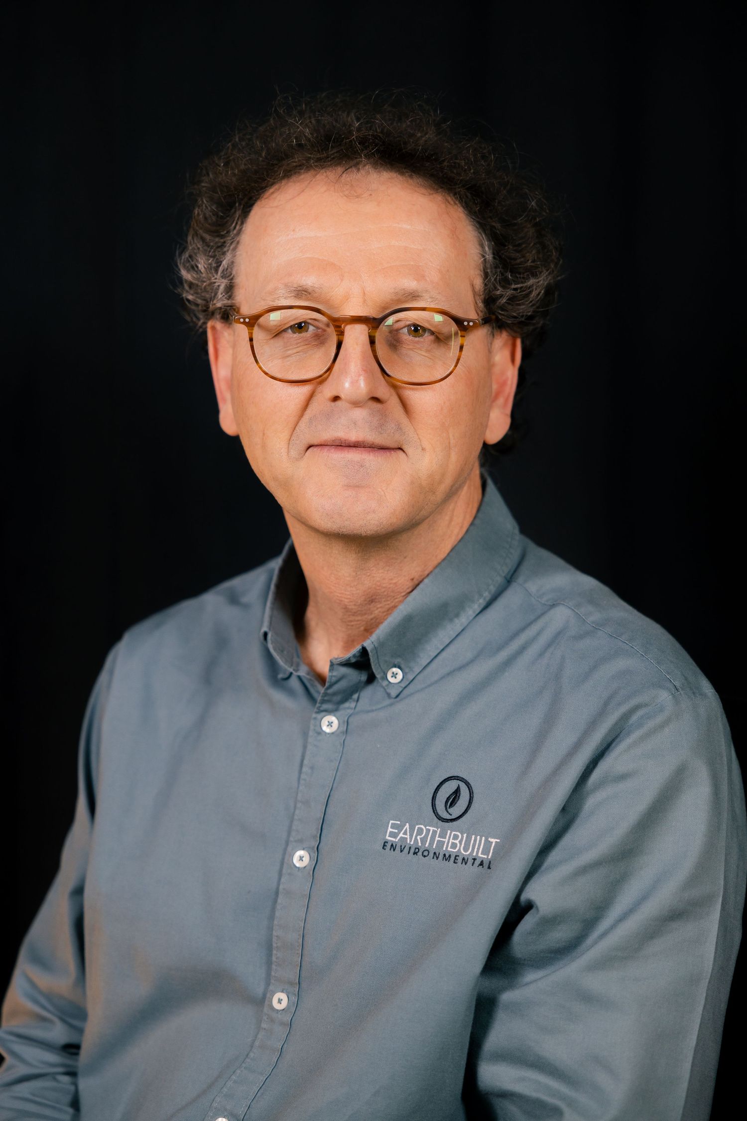 Professional headshot of man in glasses, dark backdrop studio portrait.