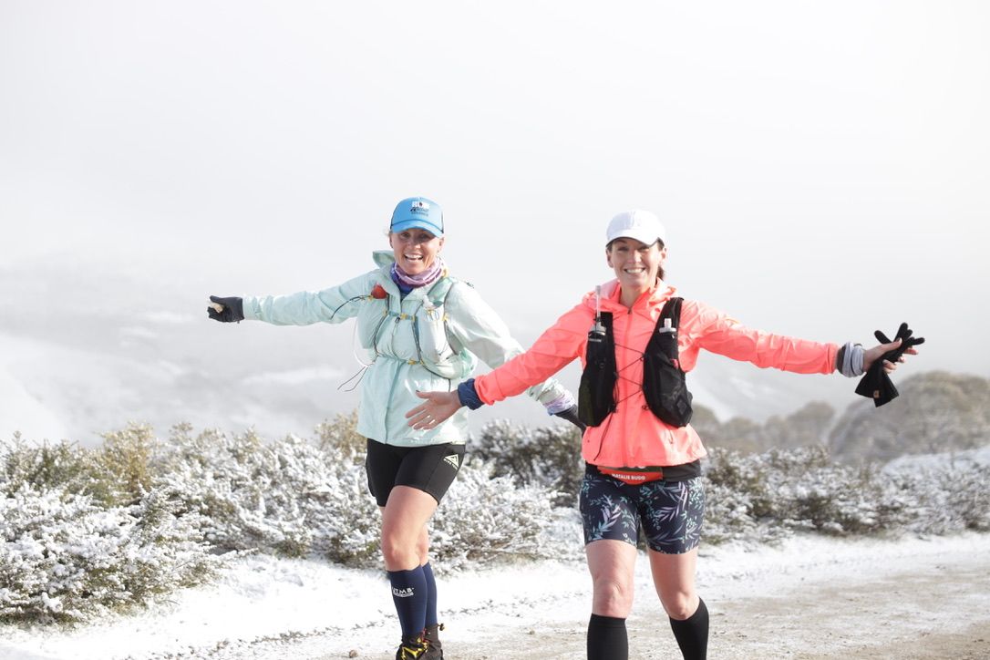 Two runners in cold weather gear smiling and posing mid-race.