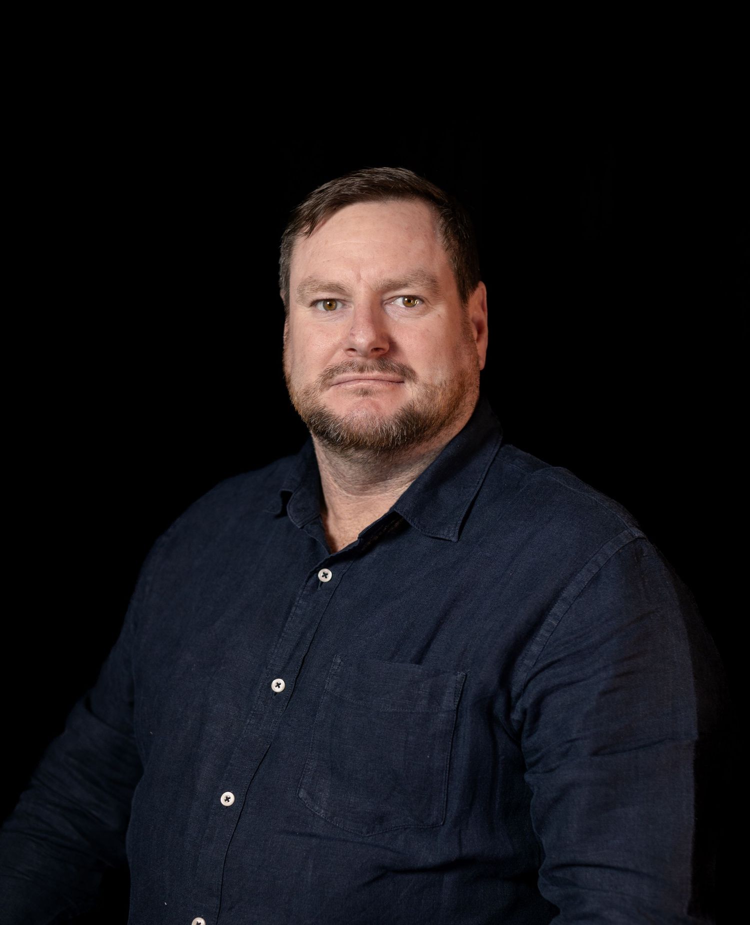 Professional headshot of man in dark shirt, photographed in studio.