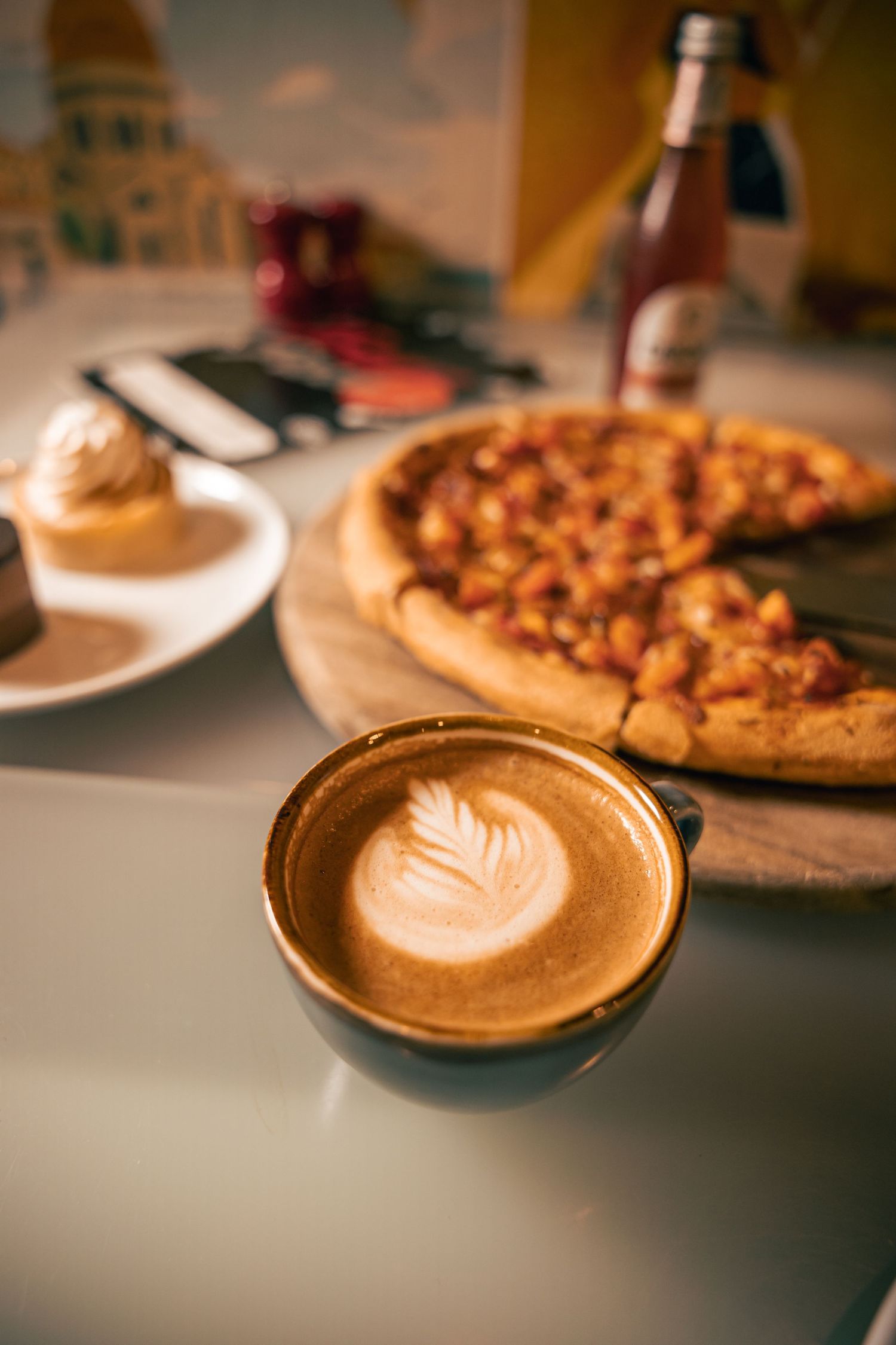 Close-up of pizza and cappuccino on café table, warm lifestyle shot.
